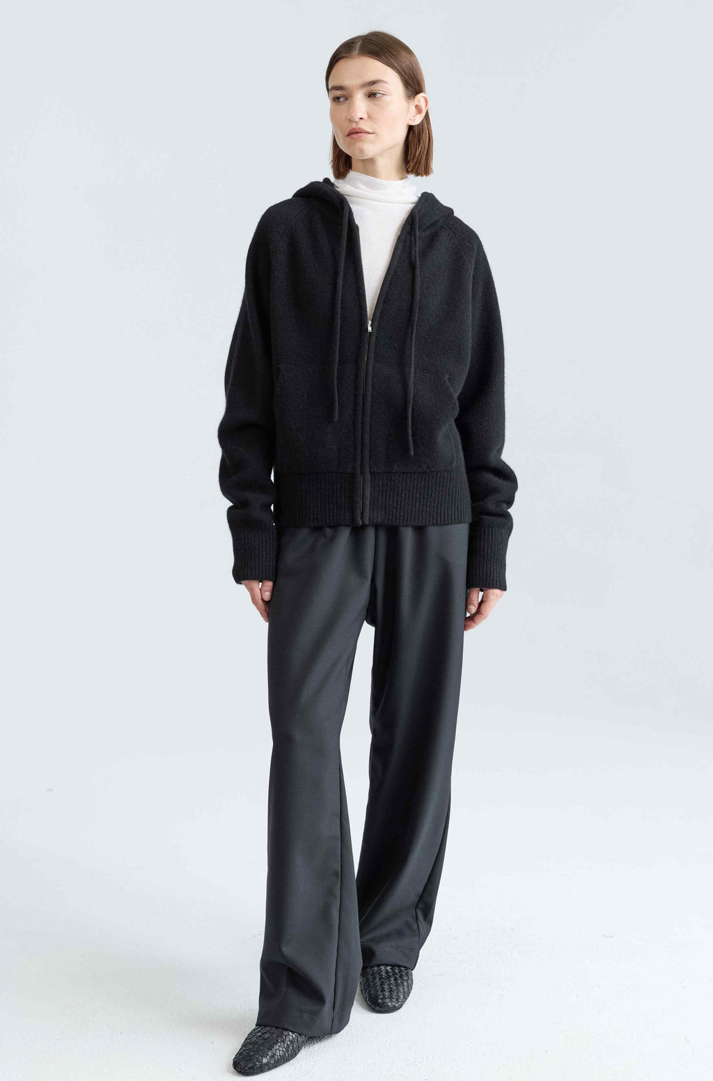 Person wearing a black hoodie and gray pants on a white background