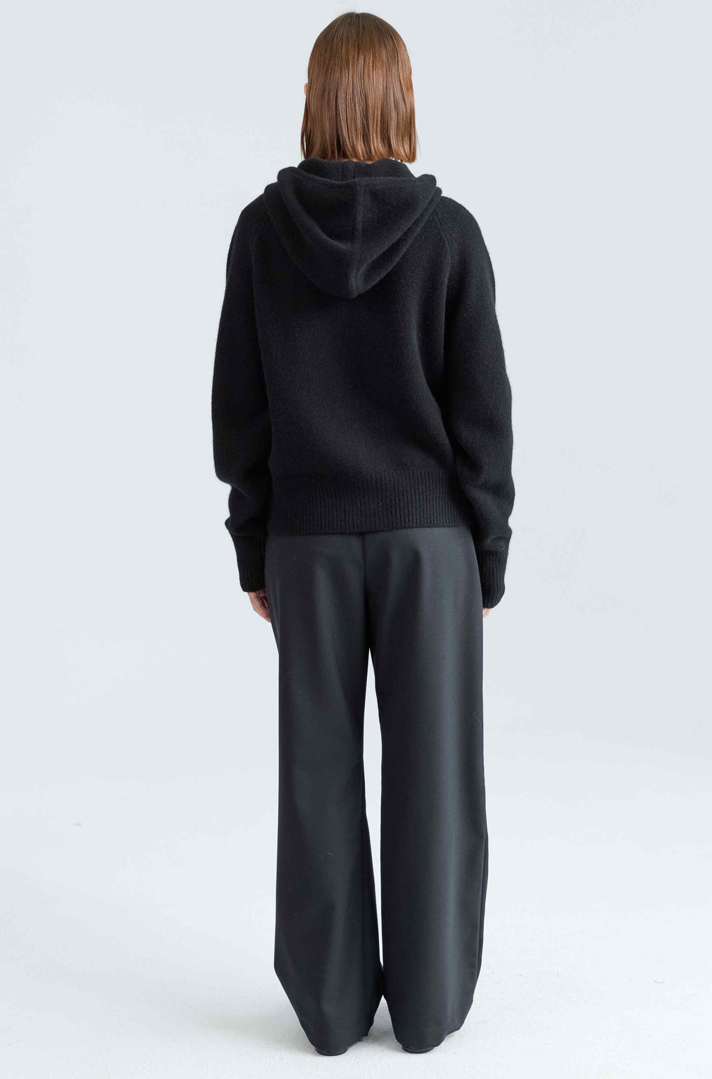 Person wearing a black hoodie and gray pants on a white background