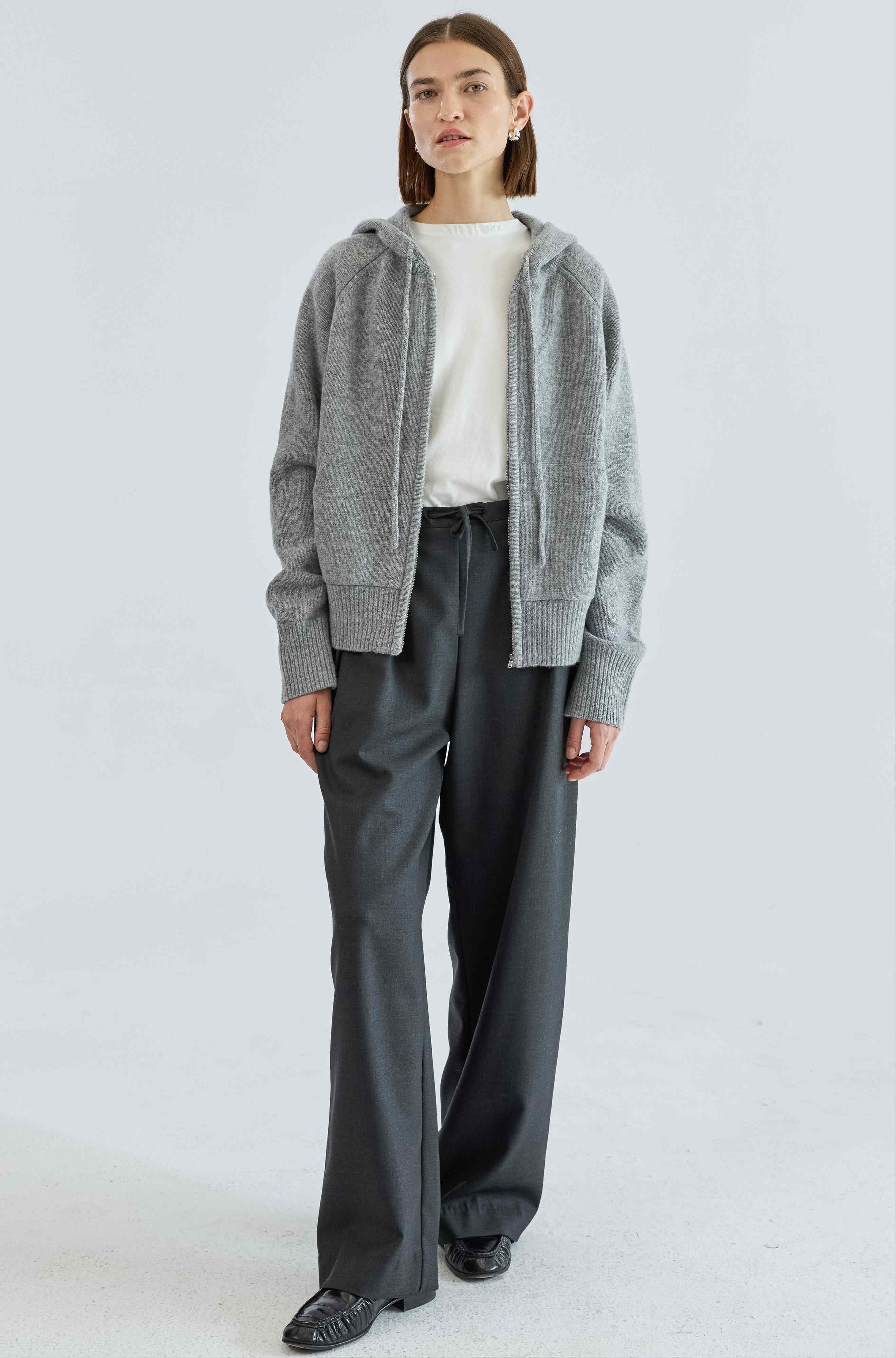 Person wearing a gray sweater, white shirt, and dark pants on a light gray background