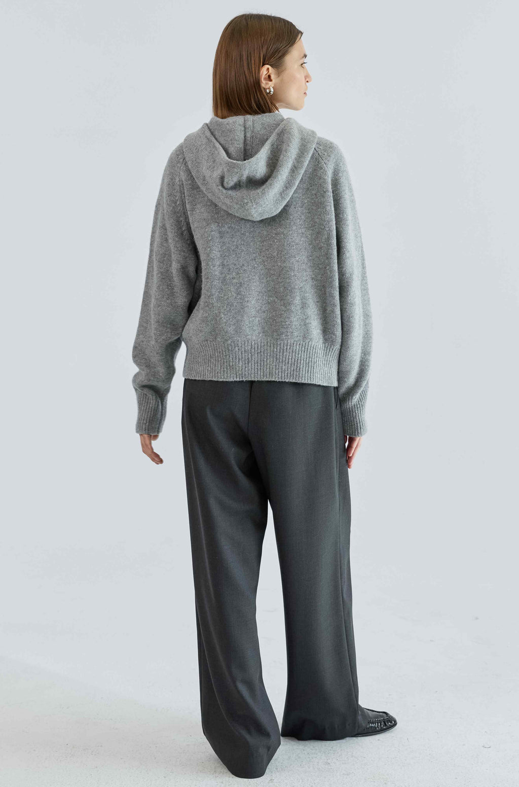 Person wearing a gray hoodie and dark pants on a light gray background