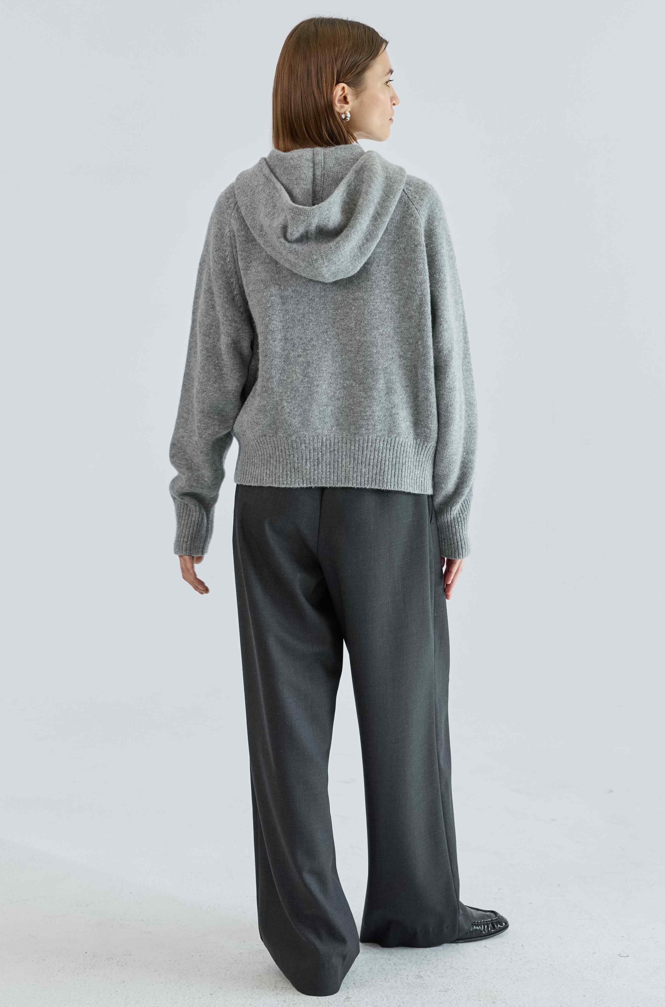 Person wearing a gray hoodie and dark pants on a light gray background