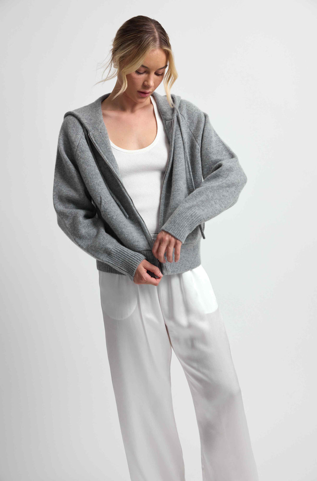 Woman wearing a gray hoodie over a white top and pants on a light gray background
