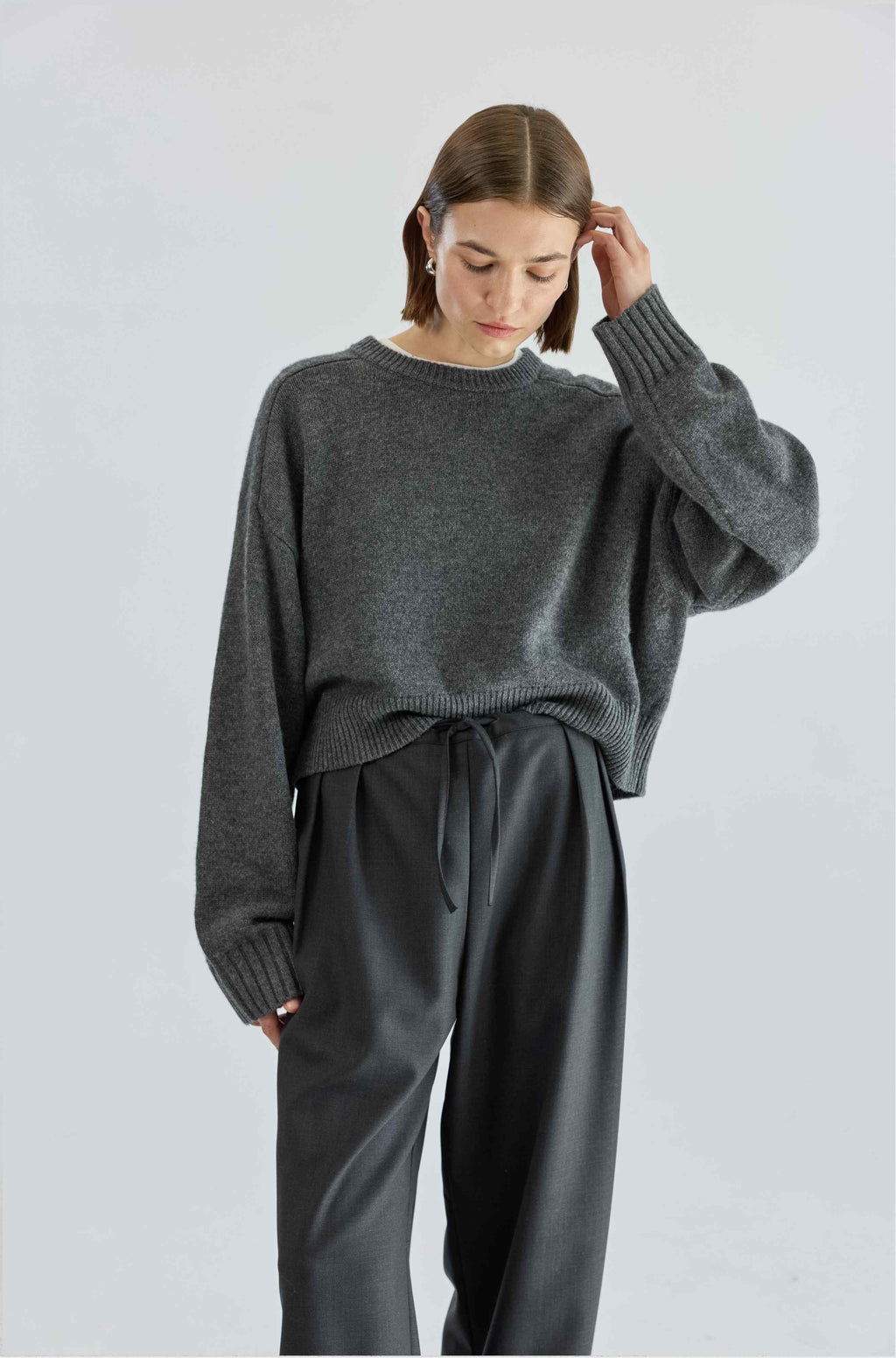 Person wearing a gray sweater and pants on a light gray background