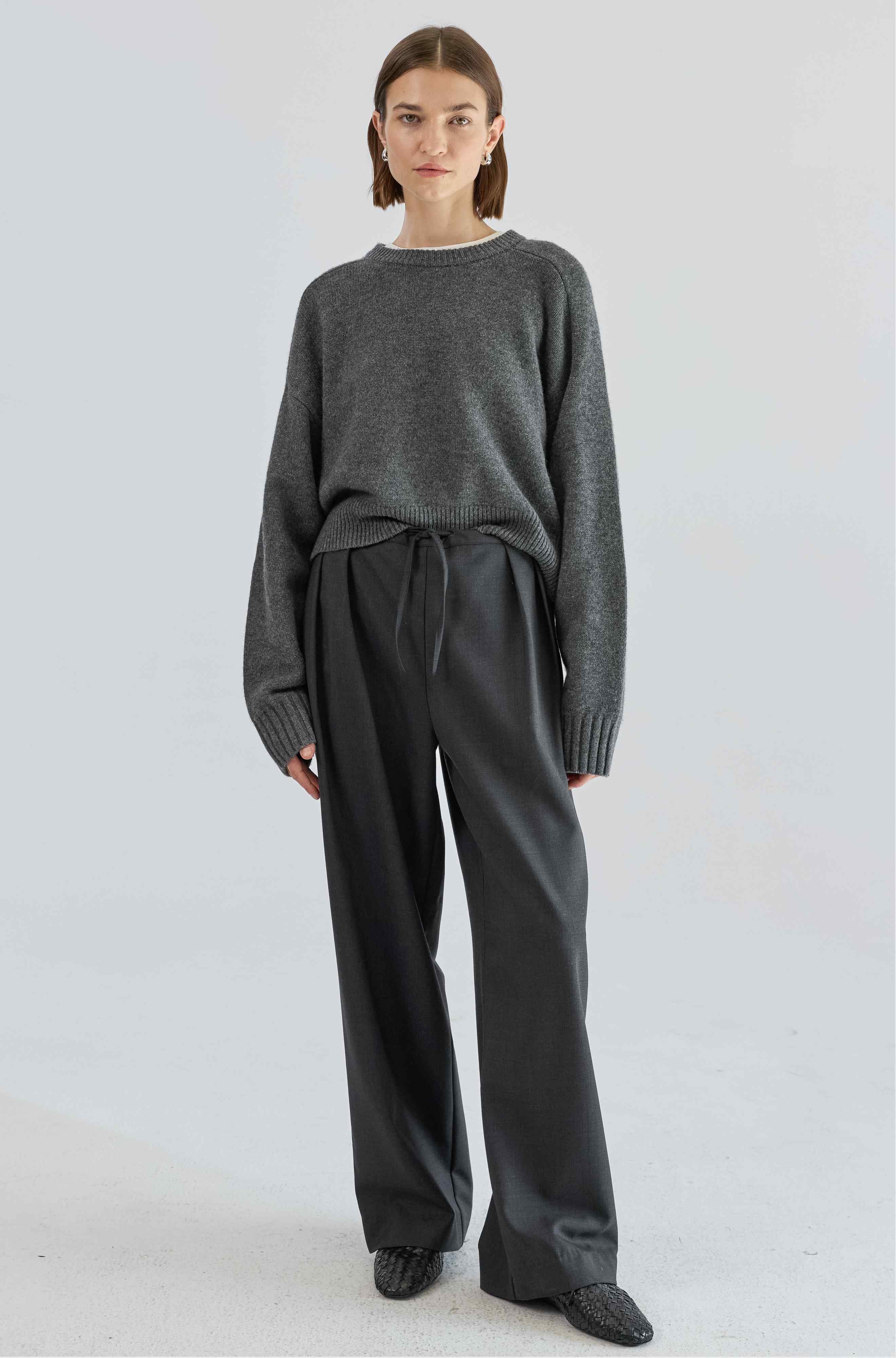 Person wearing a gray sweater and dark pants on a light gray background