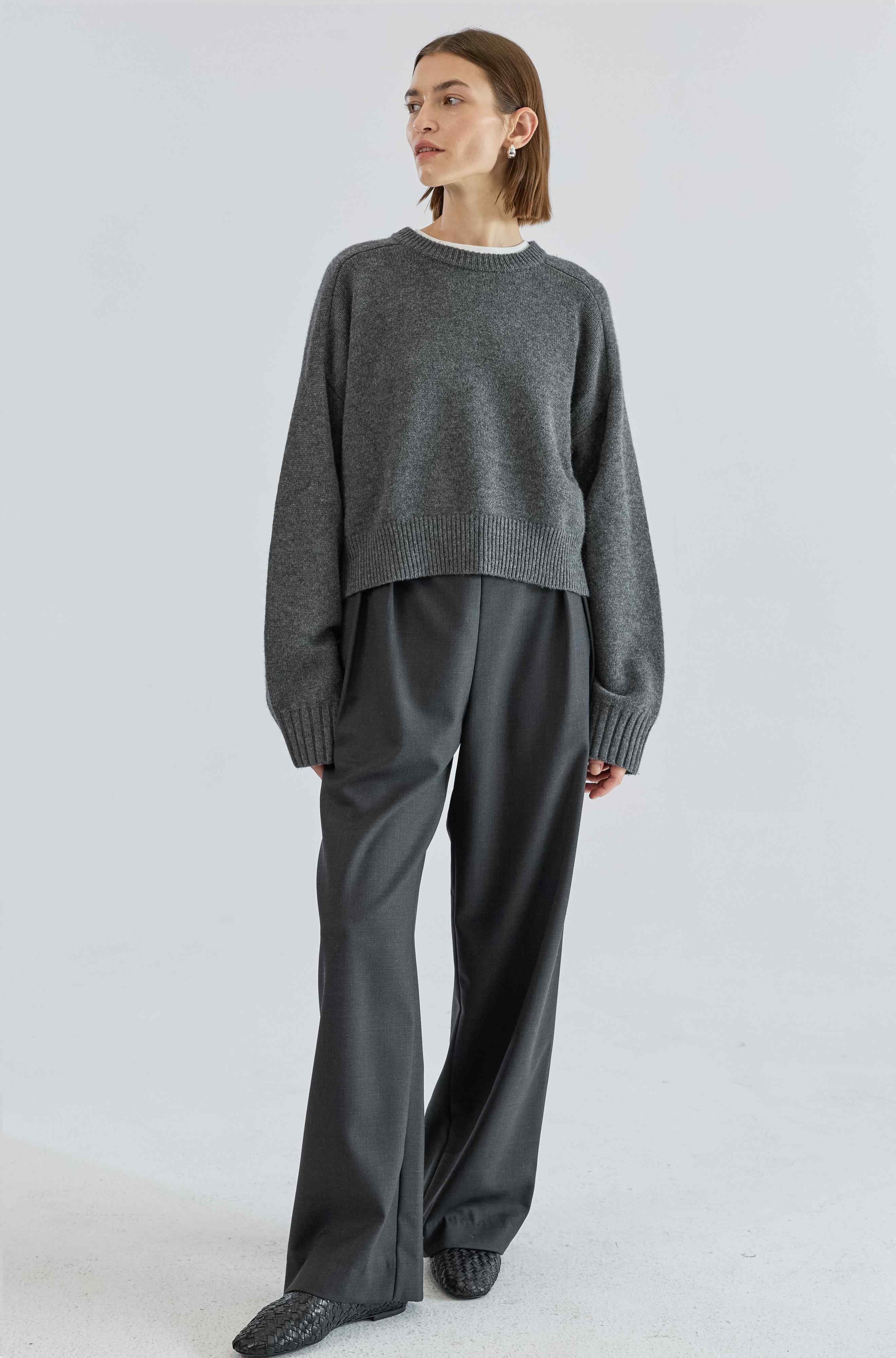 Person wearing a gray sweater and pants on a white background