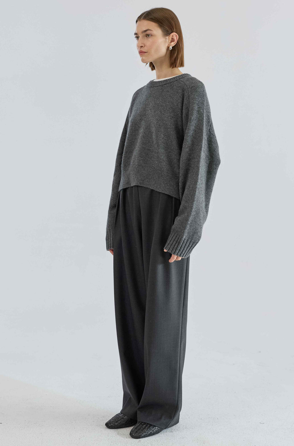 Person wearing a gray sweater and black pants on a white background