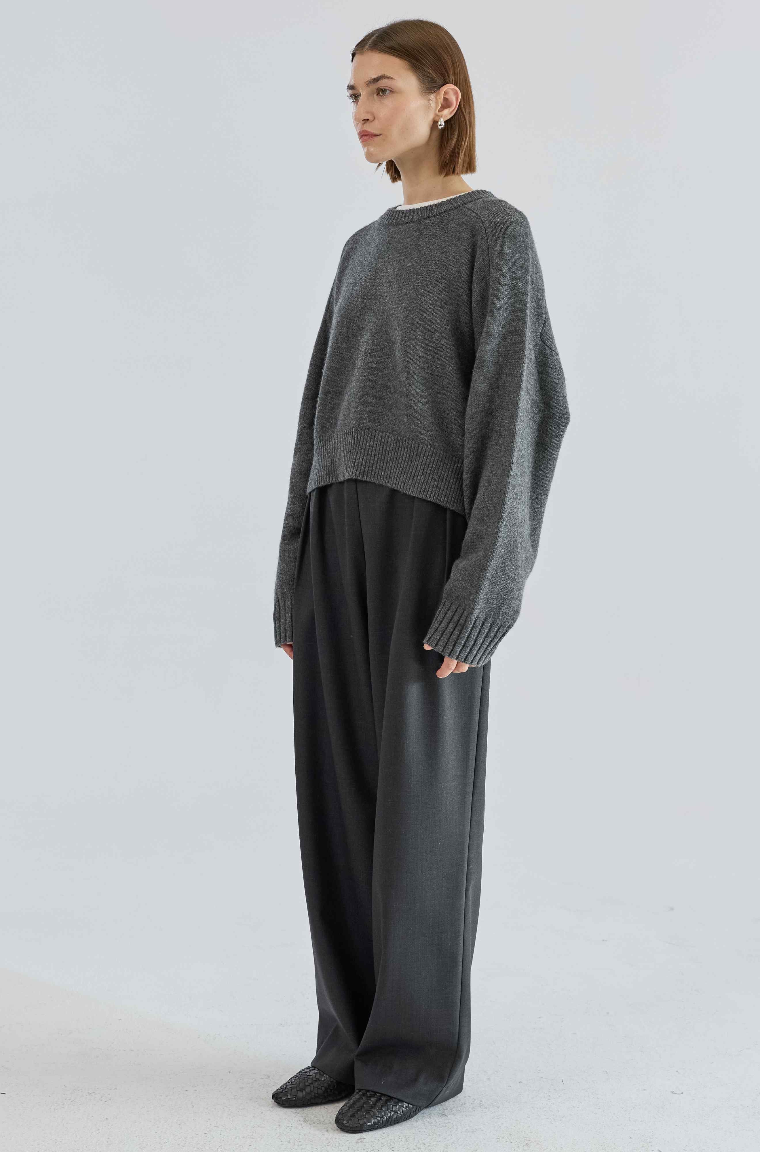 Person wearing a gray sweater and black pants on a white background