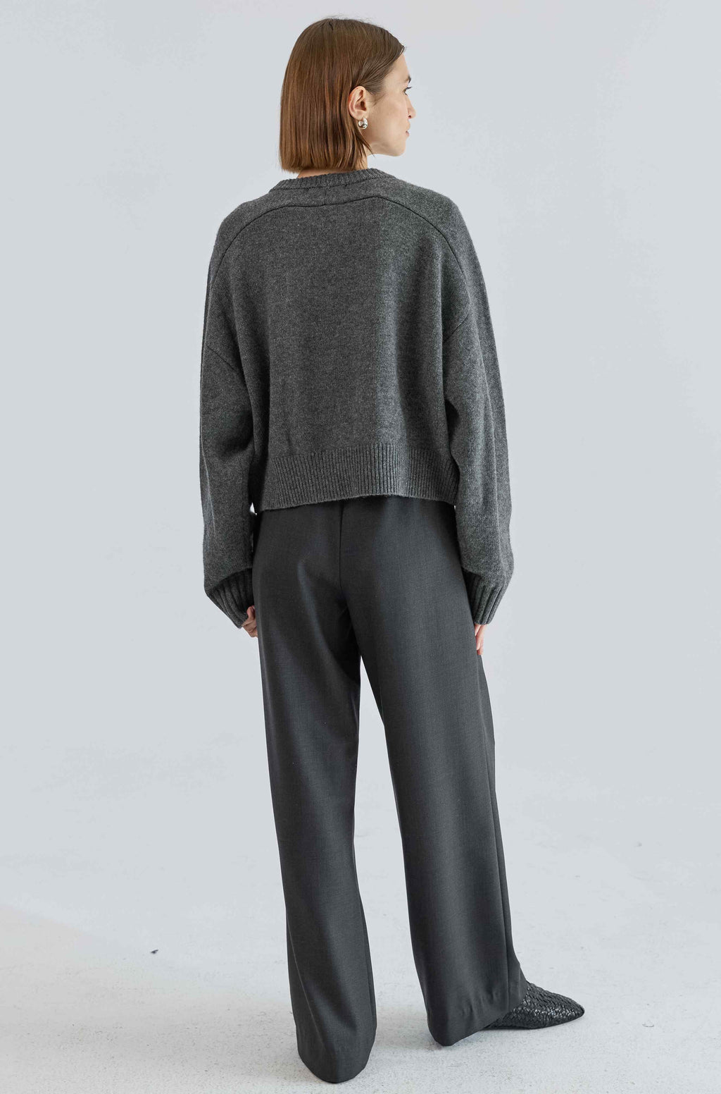 Person wearing a gray sweater and pants on a white background