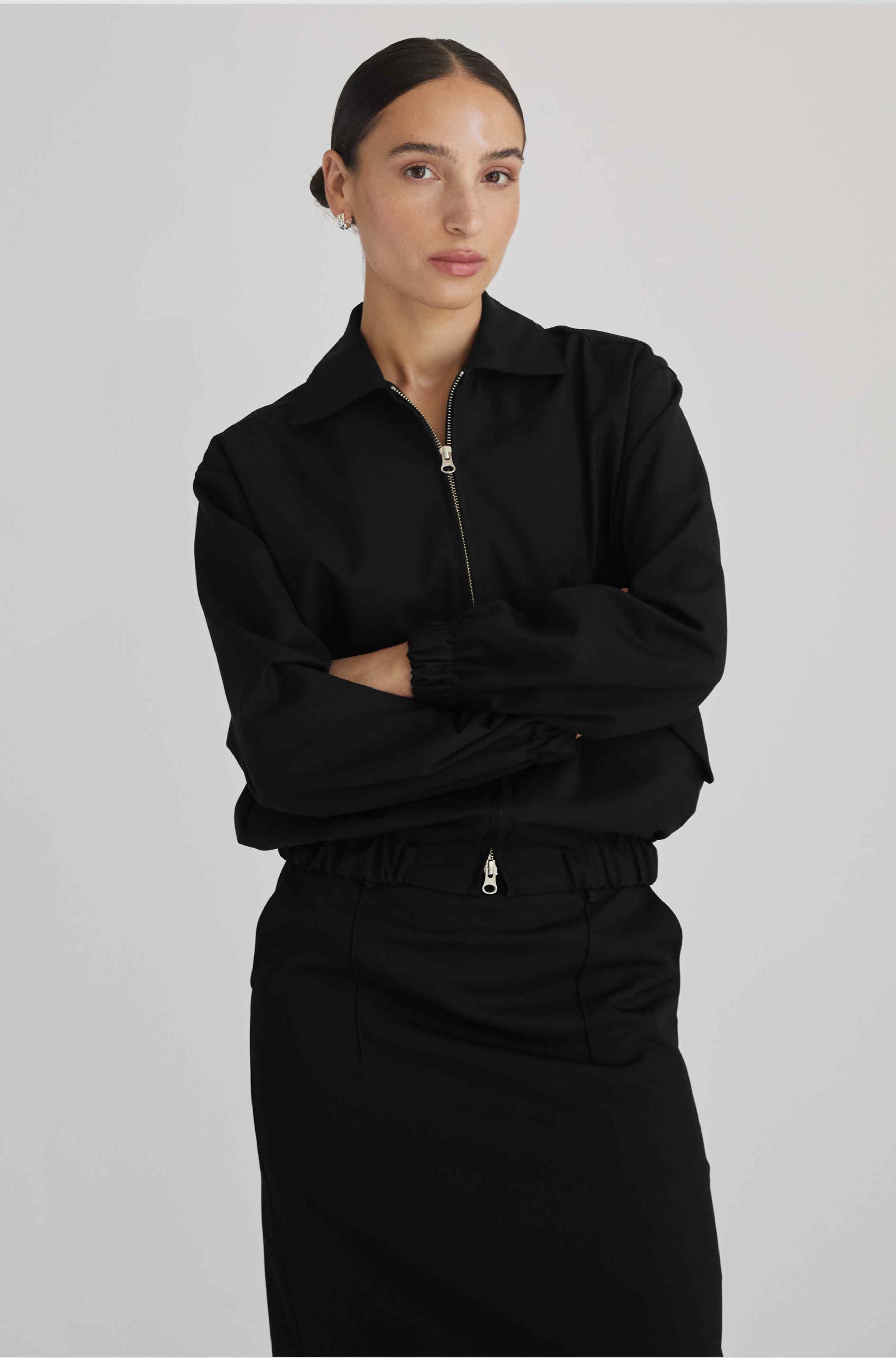 Person wearing a black outfit with a high collar on a plain background