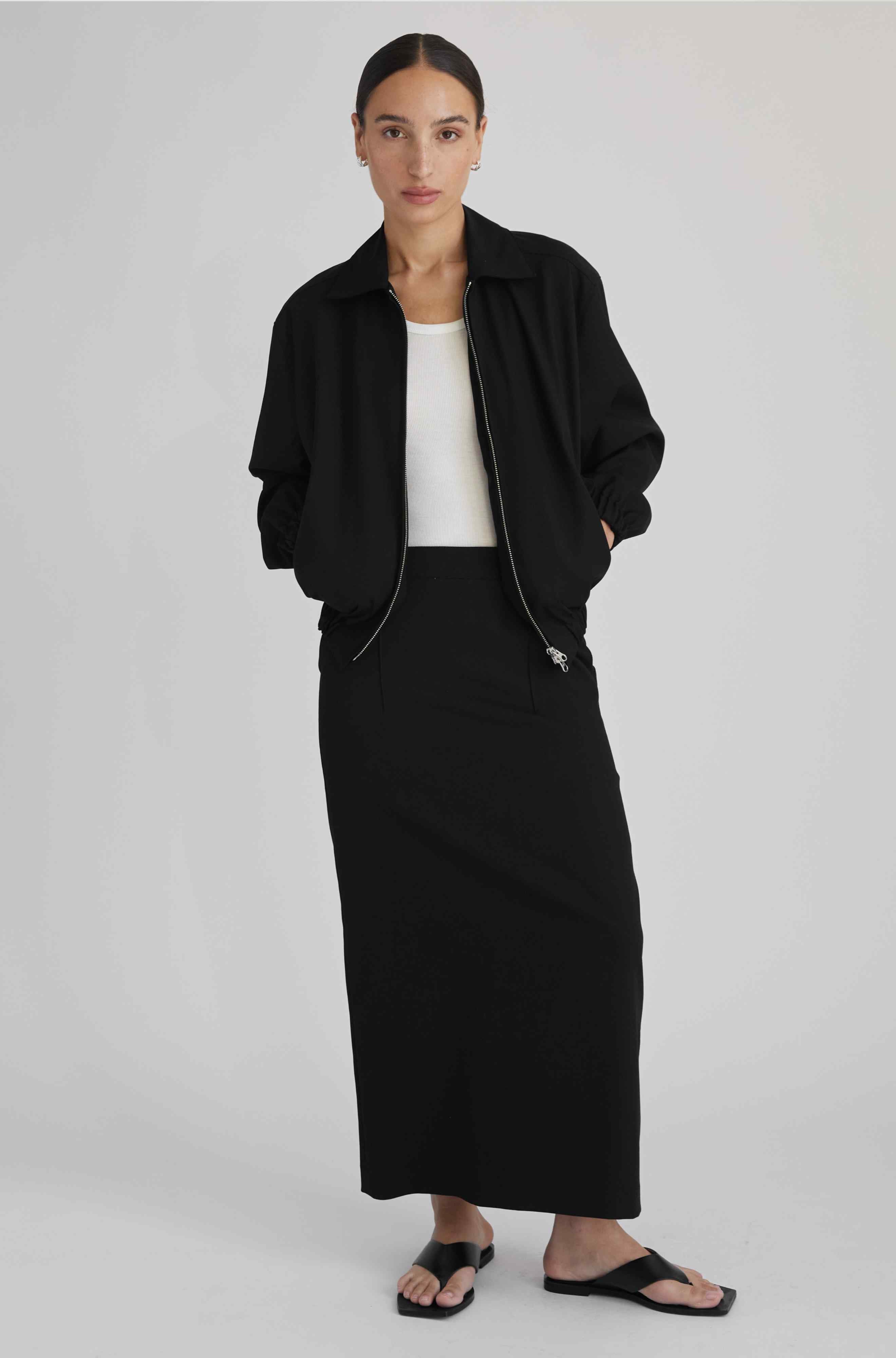 Woman wearing a black jacket and black skirt on a white background