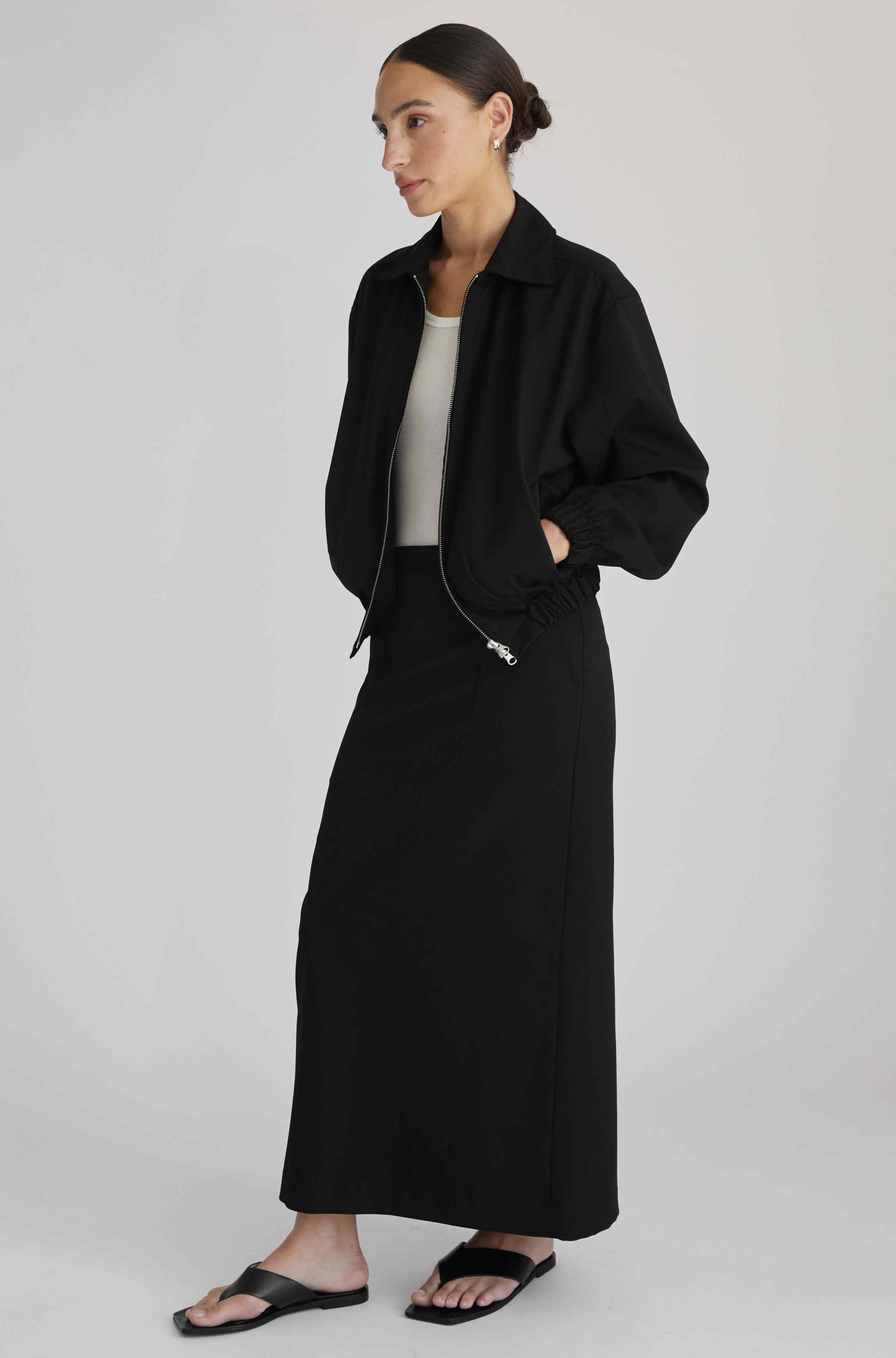 Woman wearing a black jacket and black pants on a plain background