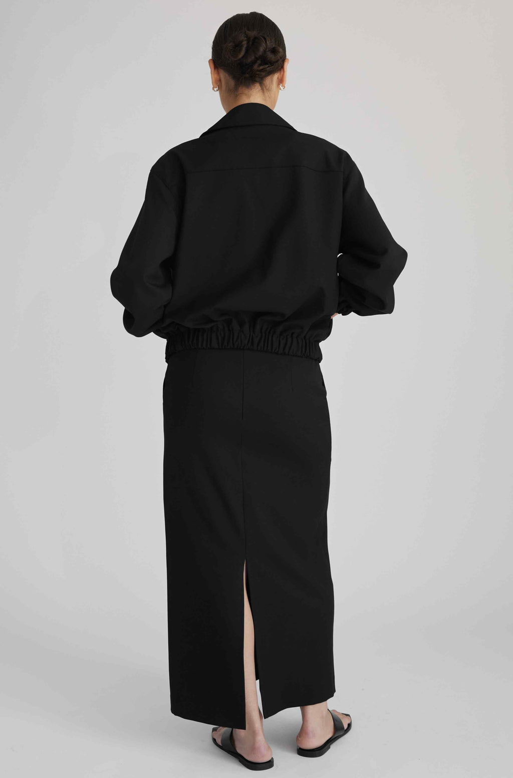 Person wearing a black outfit with a long skirt on a plain background
