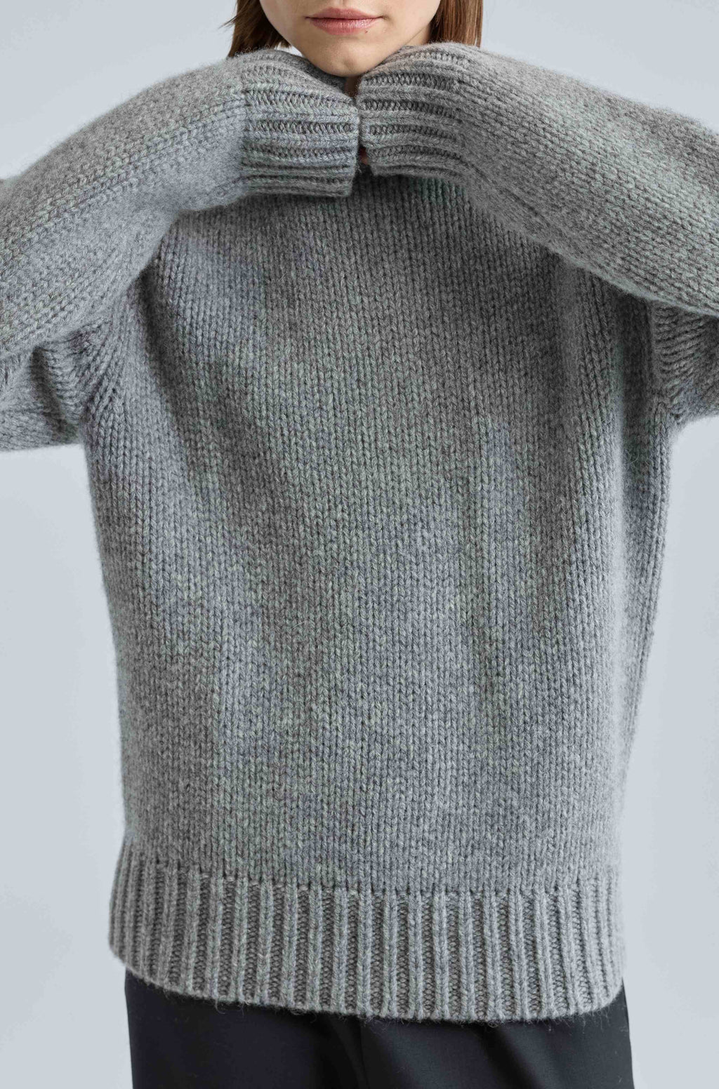Person wearing a gray knitted sweater against a light background