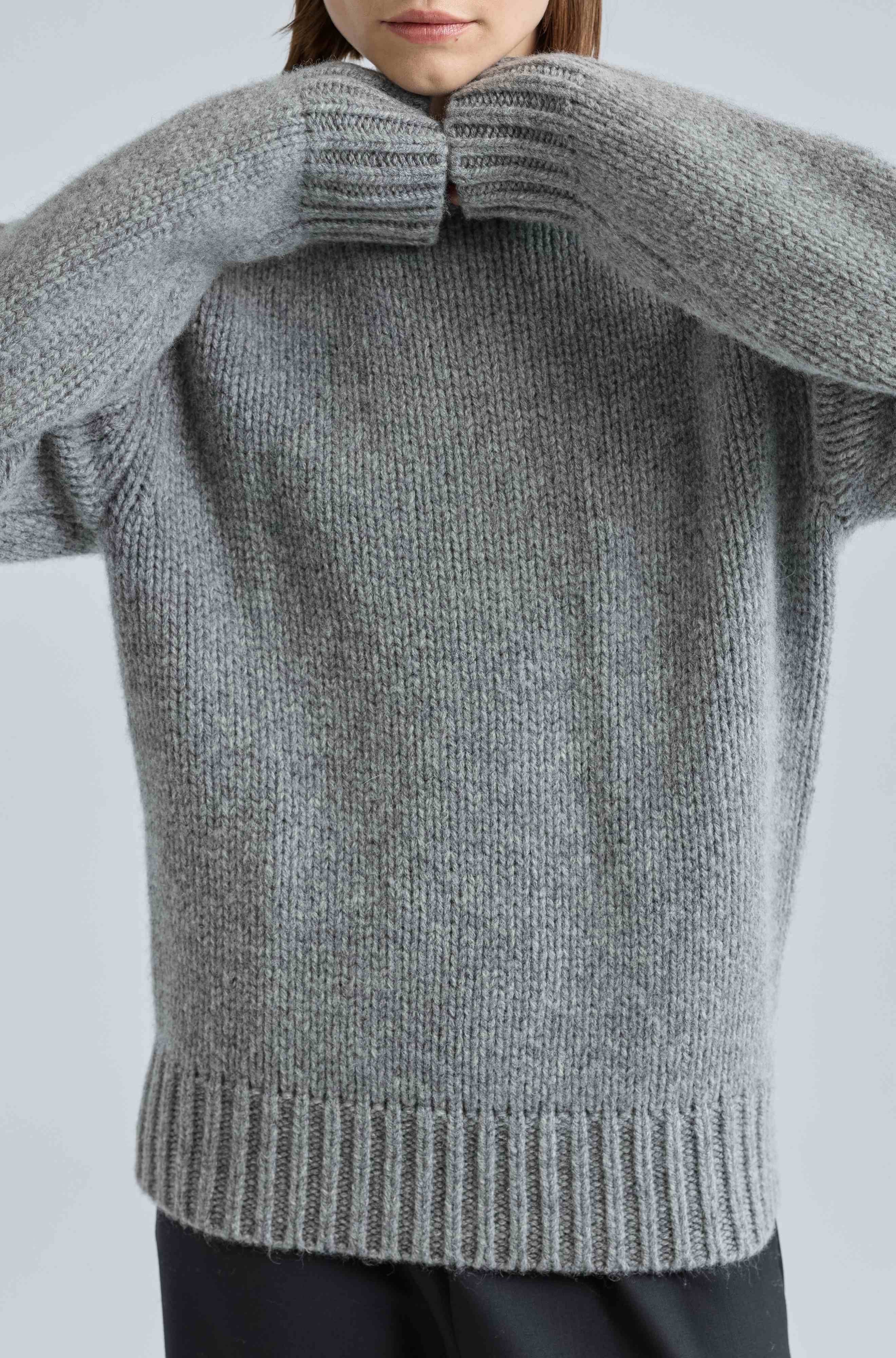 Person wearing a gray knitted sweater against a light background
