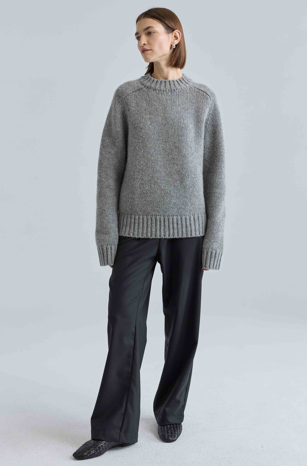 Person wearing a gray sweater and black pants on a light gray background