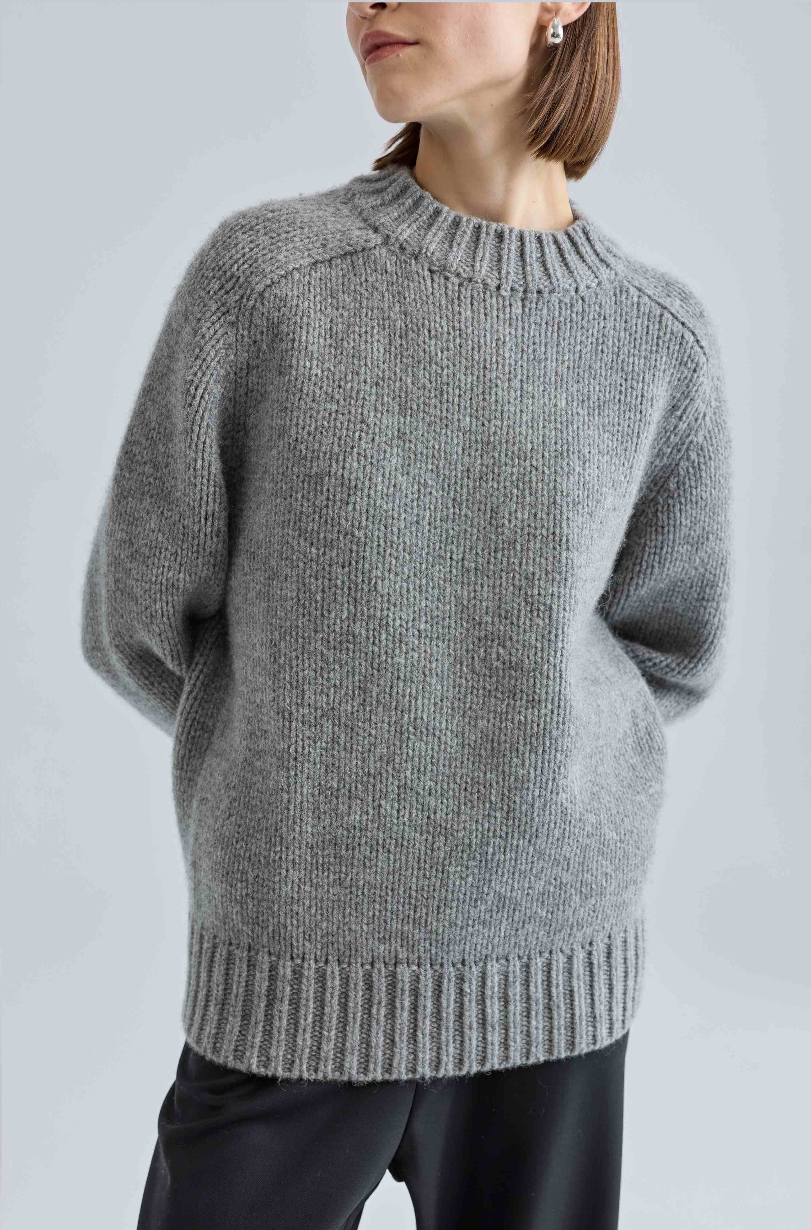 Person wearing a gray knitted sweater against a light gray background