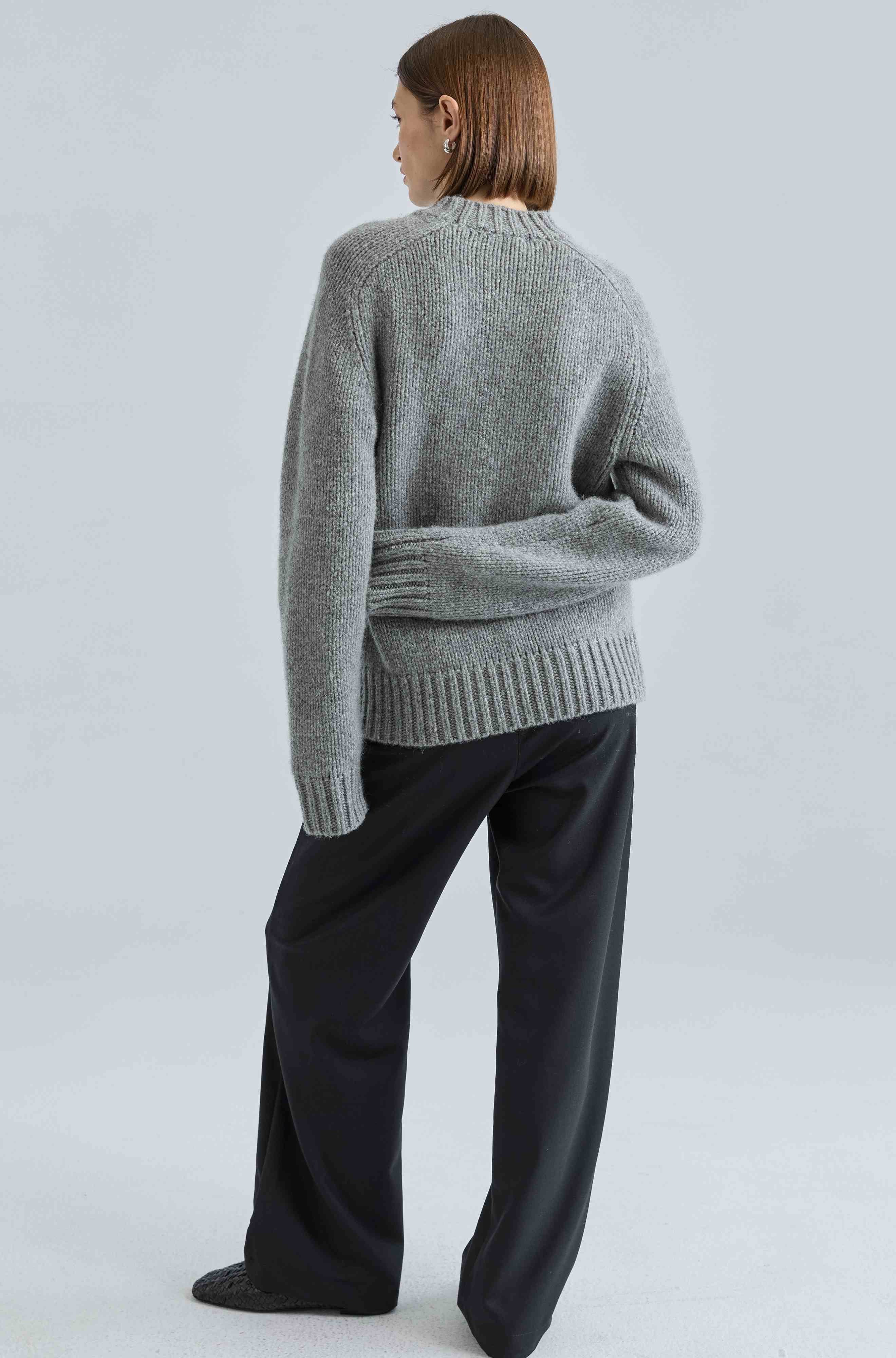 Person wearing a gray sweater and black pants on a light gray background