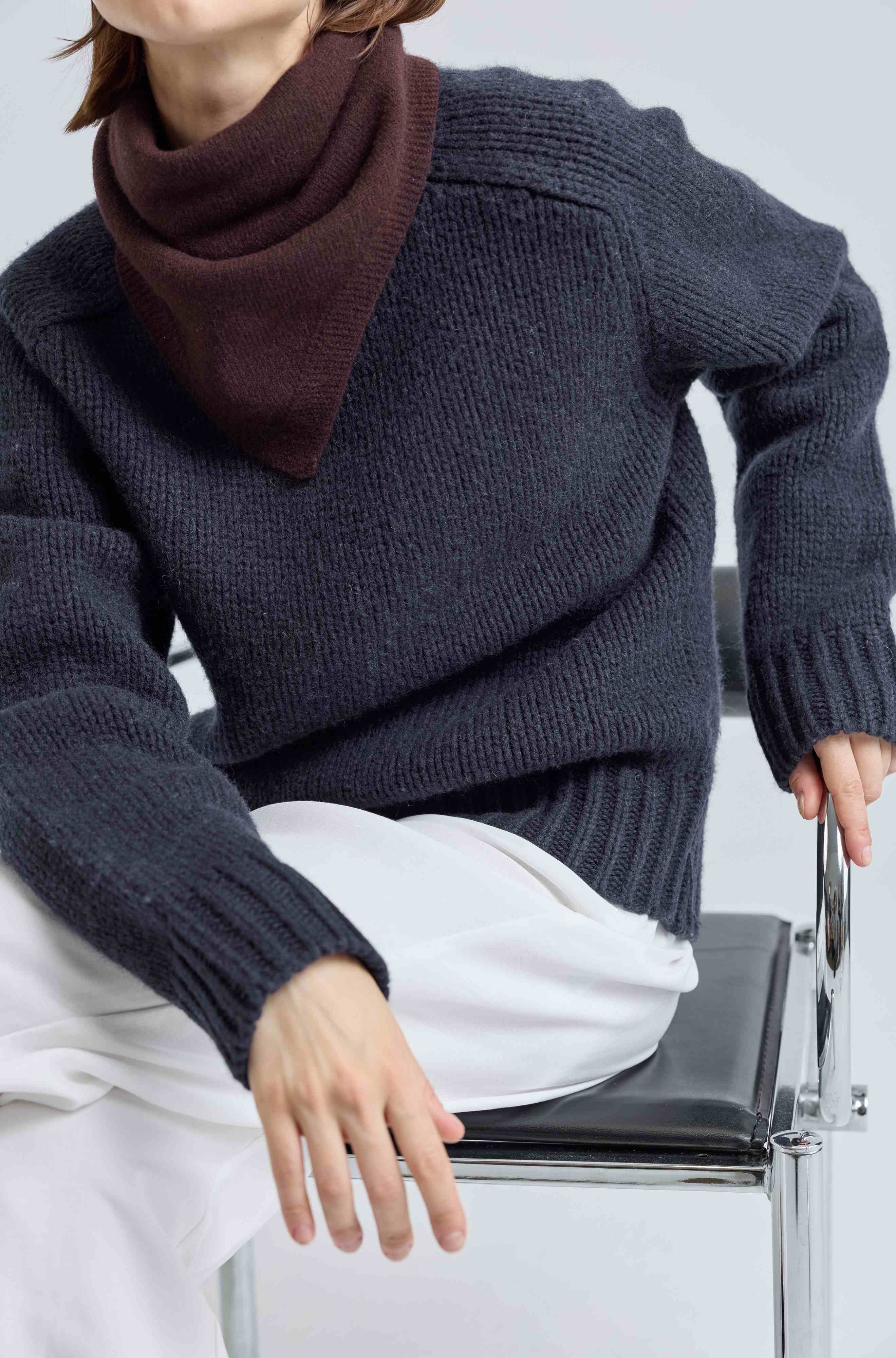 Person wearing a dark blue sweater and brown scarf sitting on a chair.