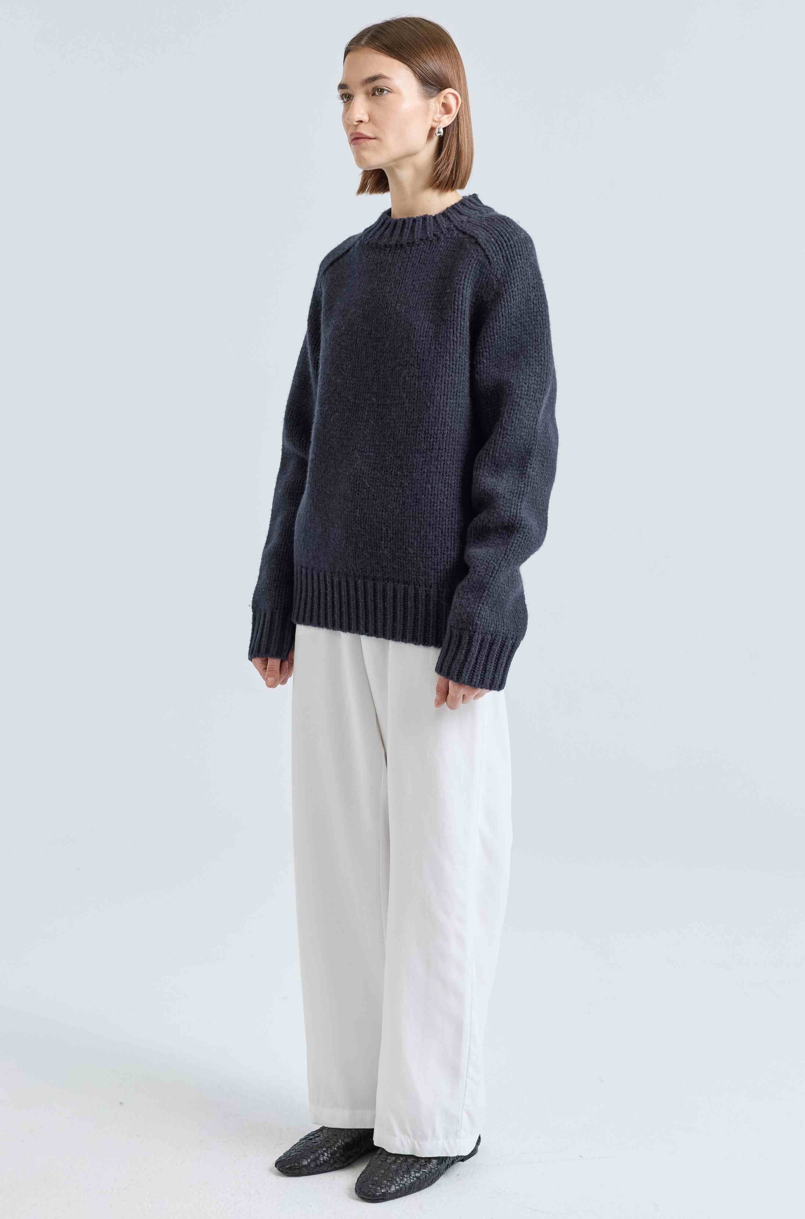Person wearing a dark blue sweater and white pants on a light gray background