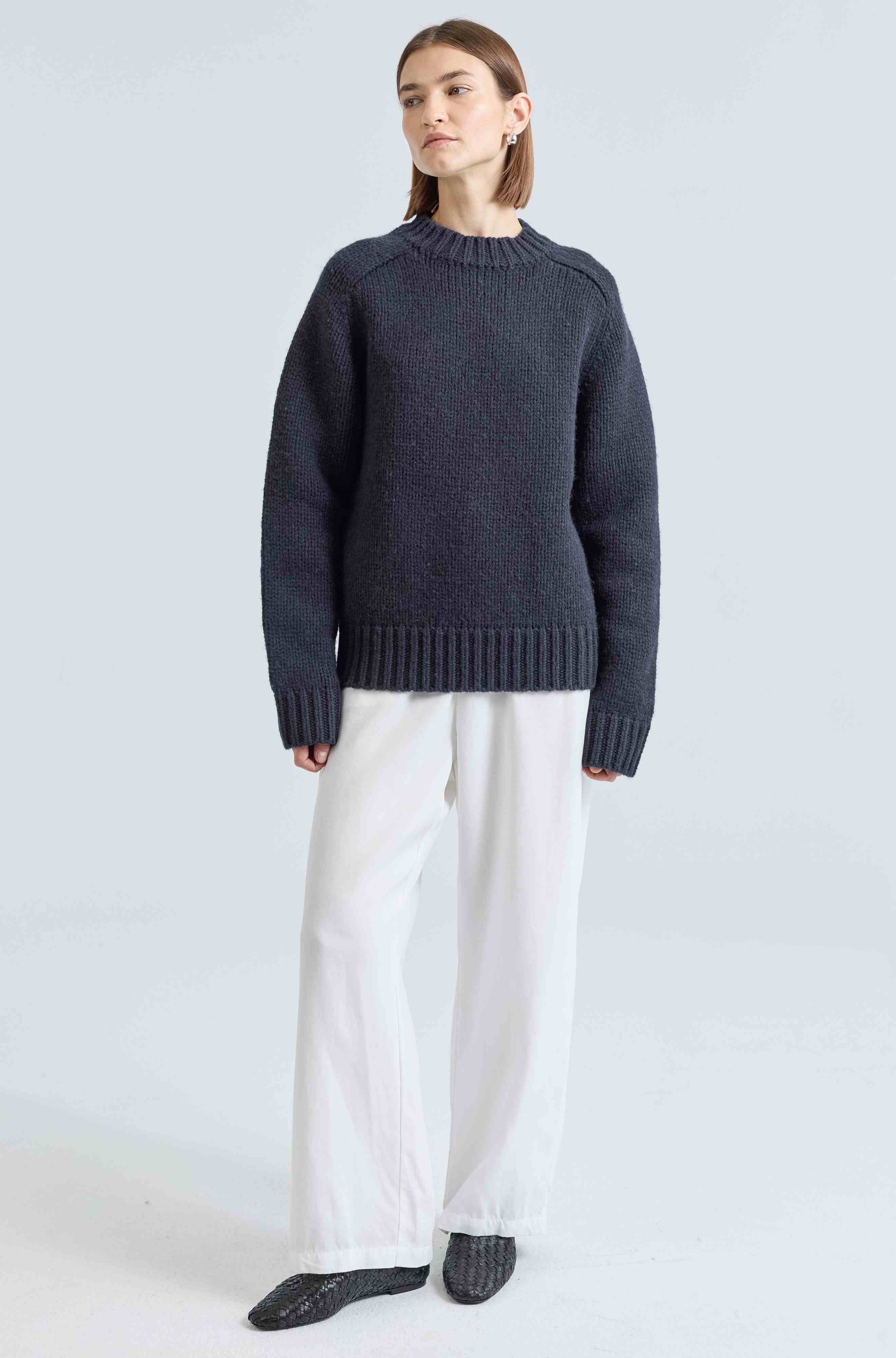 Person wearing a dark blue sweater and white pants on a light gray background