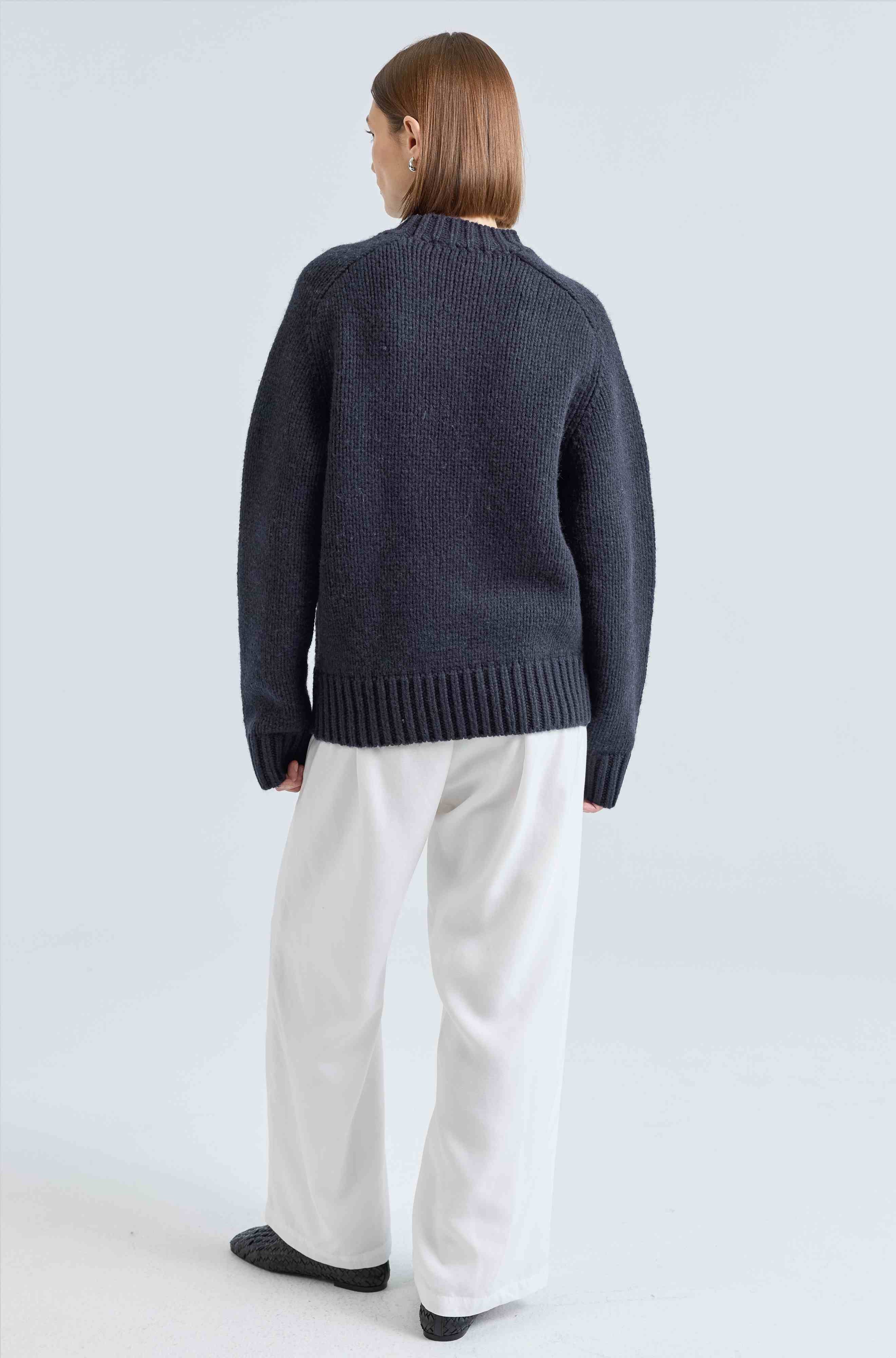 Person wearing a dark blue sweater and white pants on a light gray background