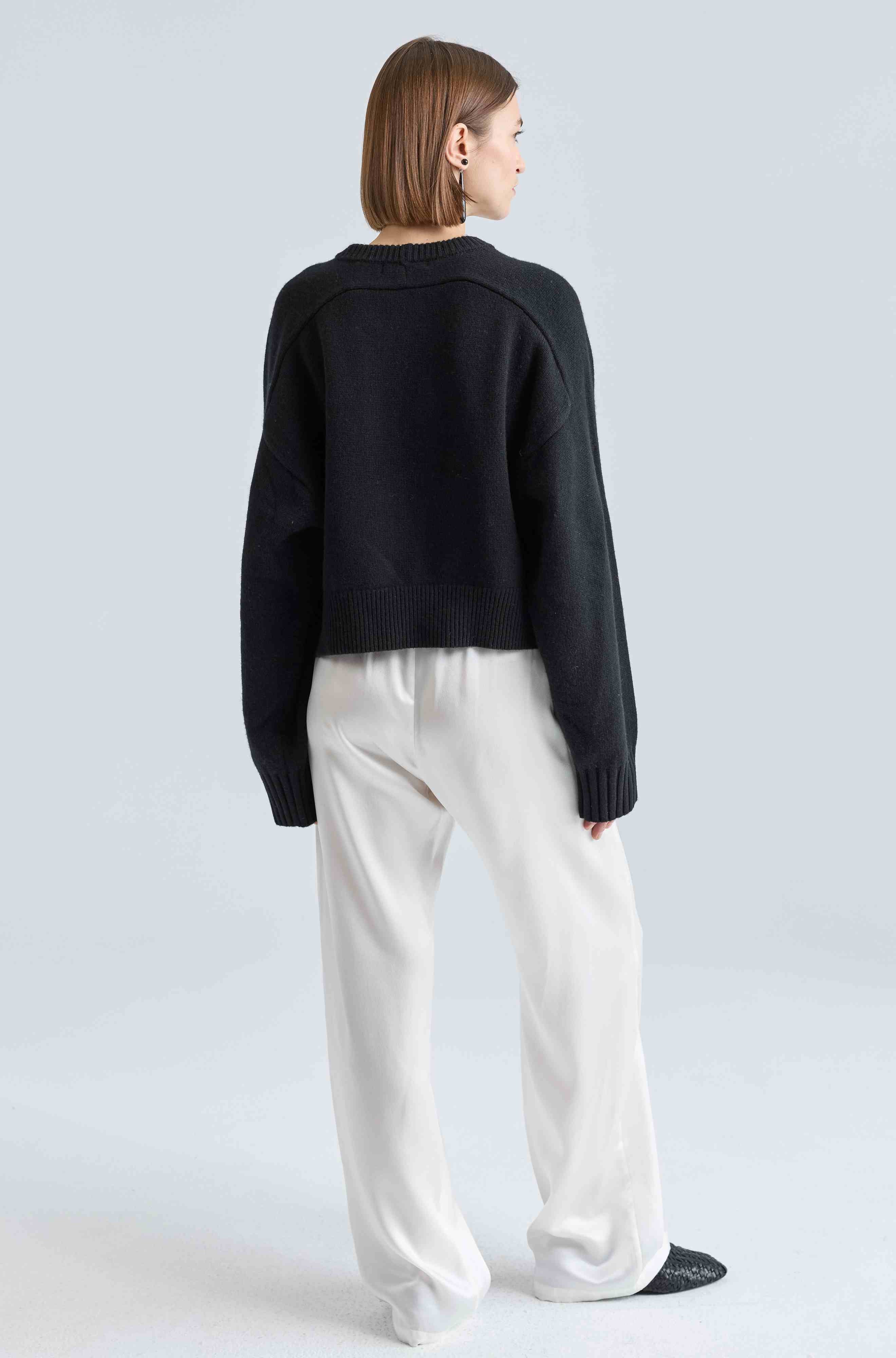 Person wearing a black sweater and white pants on a light gray background