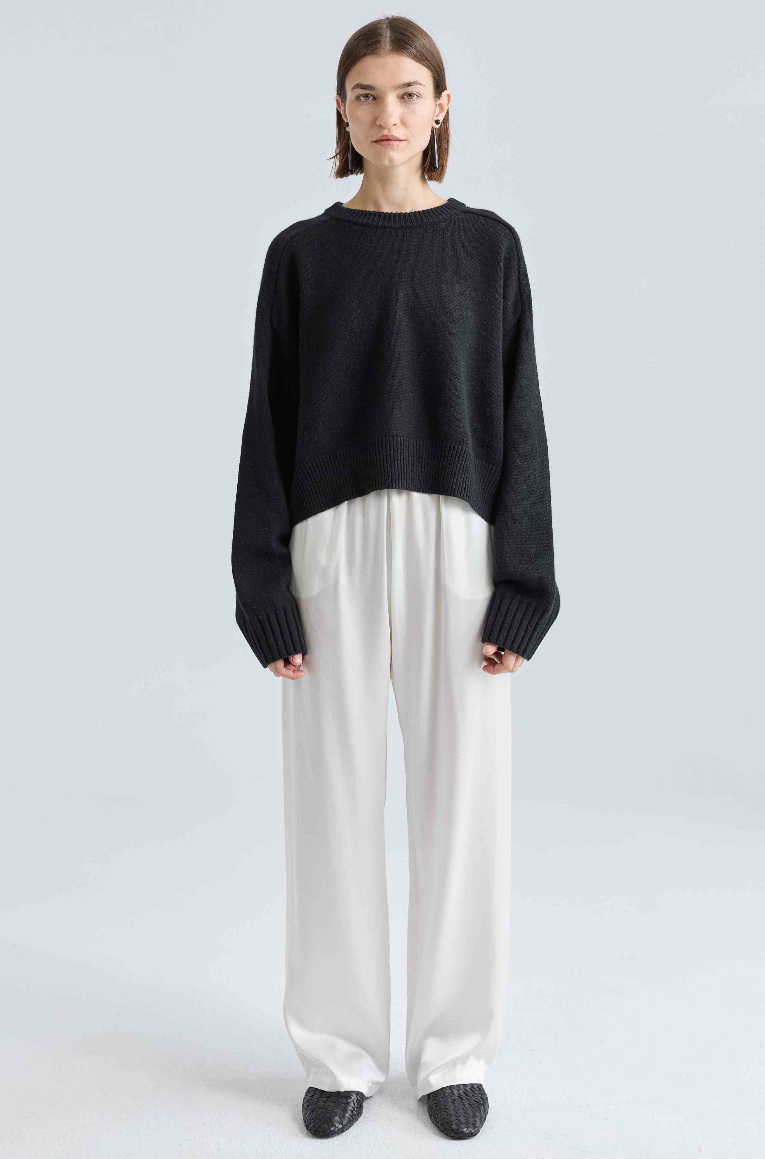 Person wearing a black sweater and white pants on a light gray background