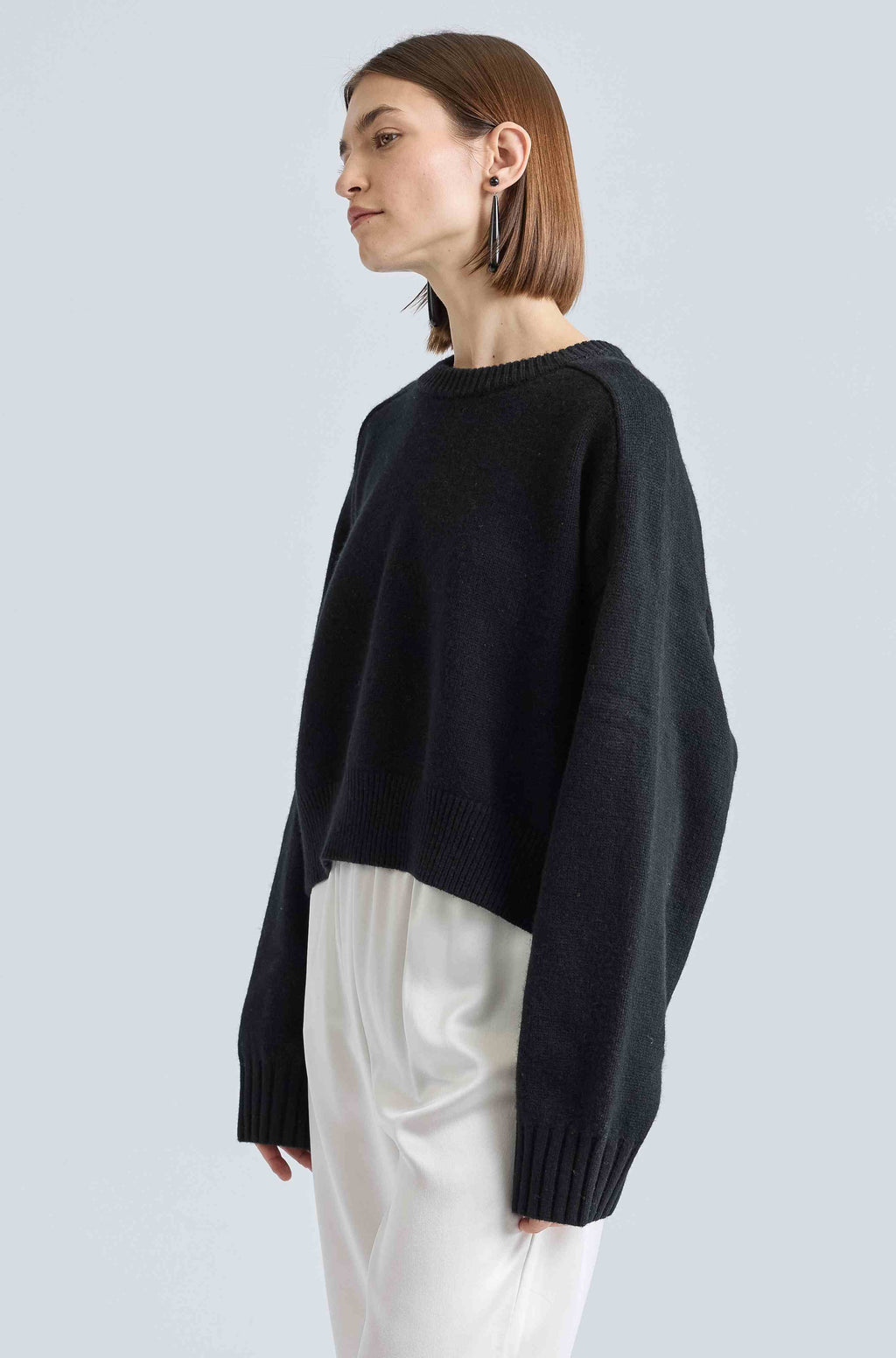 Person wearing a black sweater and white pants on a light gray background