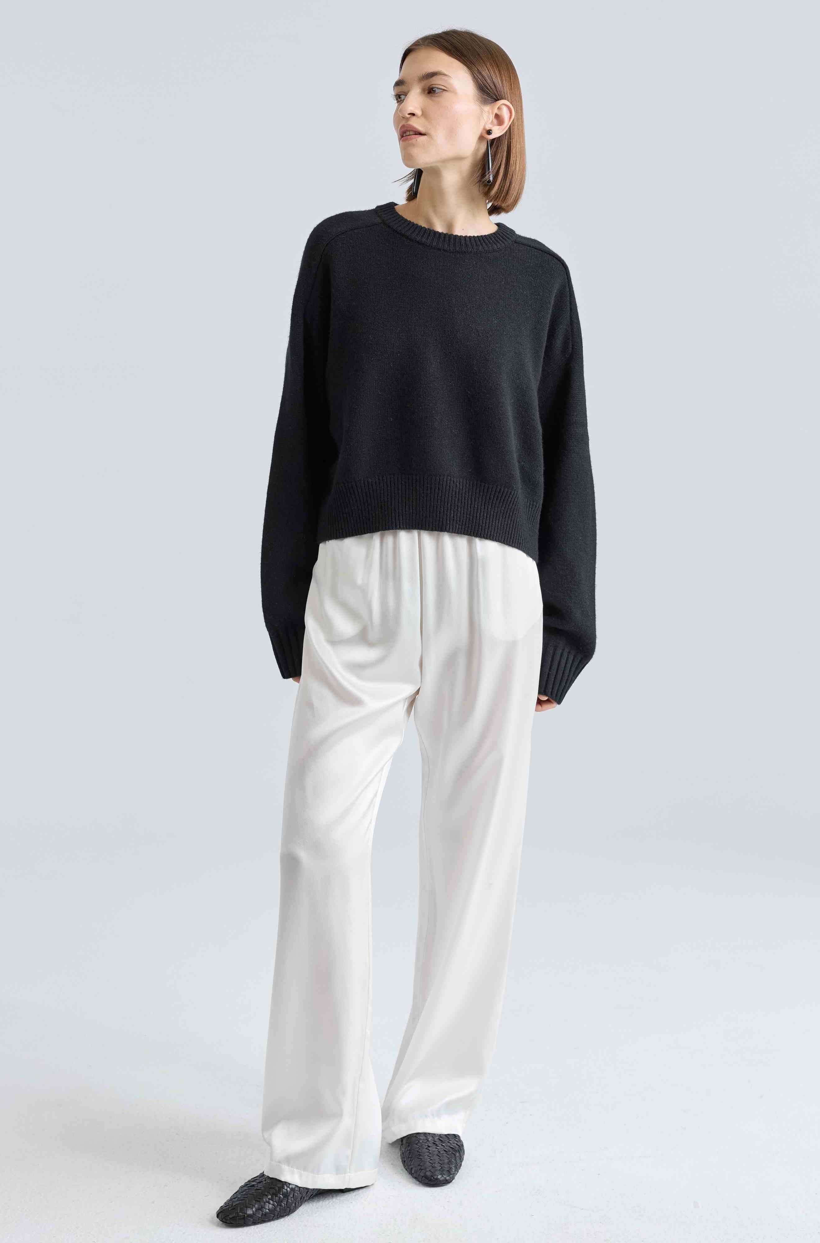 Person wearing a black sweater and white pants on a light gray background