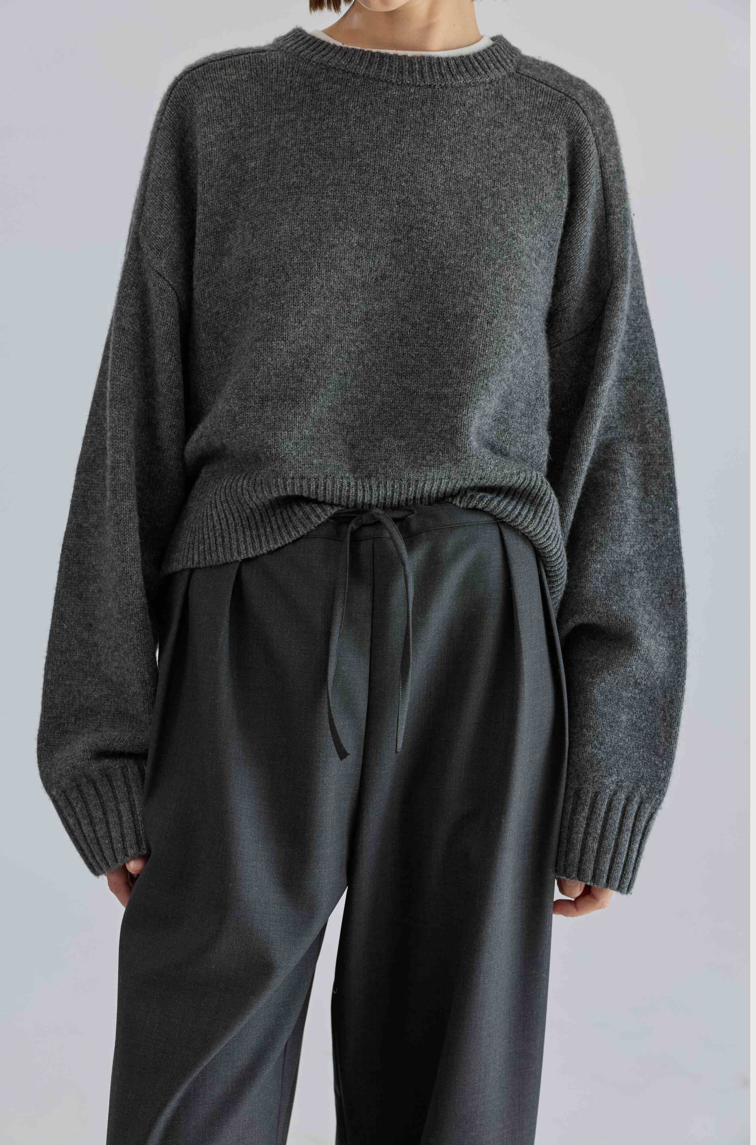 Person wearing a dark gray sweater and matching pants on a light gray background