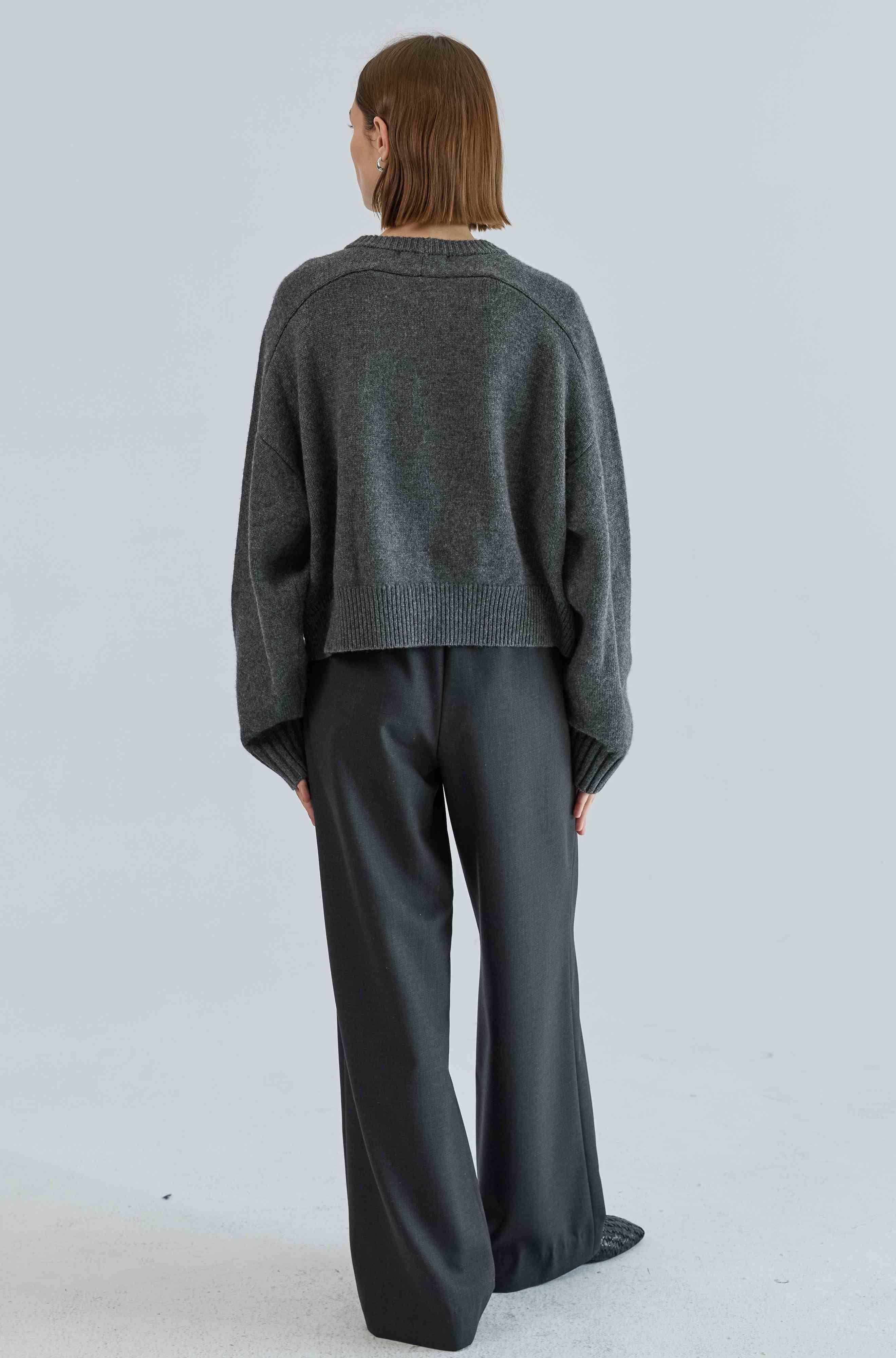 Person wearing a gray sweater and black pants on a light gray background