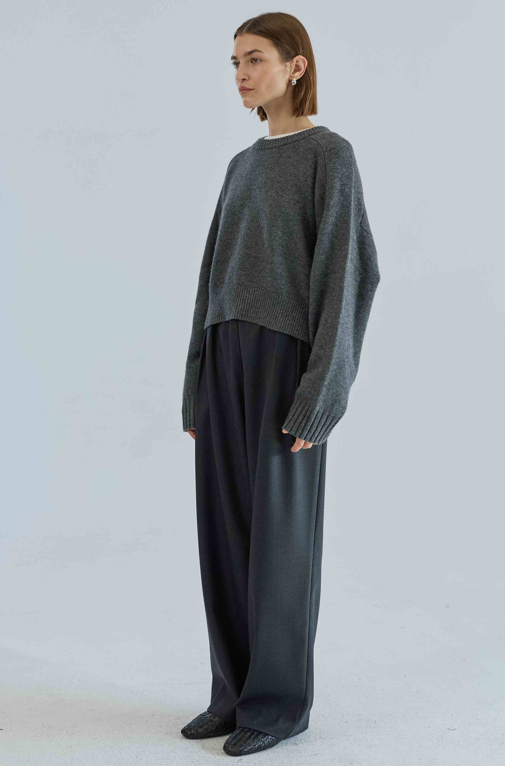 Person wearing a dark gray sweater and black pants on a light gray background
