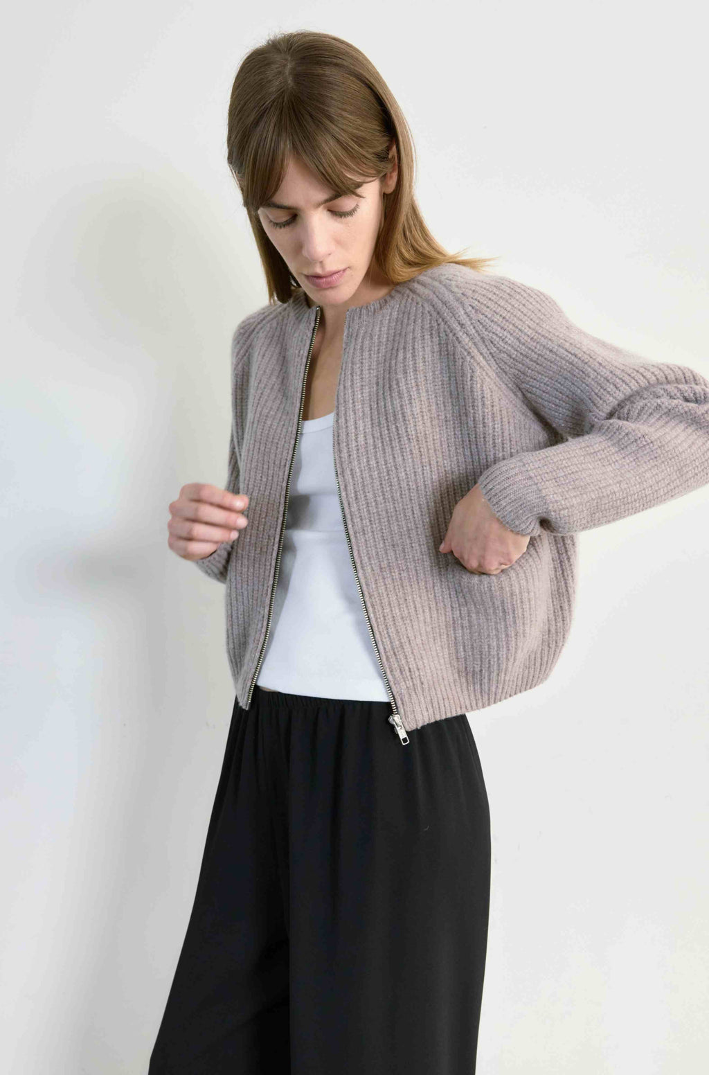 Woman wearing a light beige ribbed knit cardigan over a white top and black pants on a white background