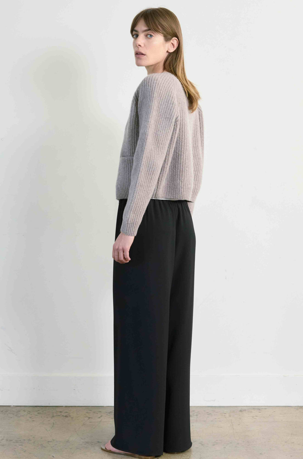 Woman wearing a light beige sweater and black pants against a white background
