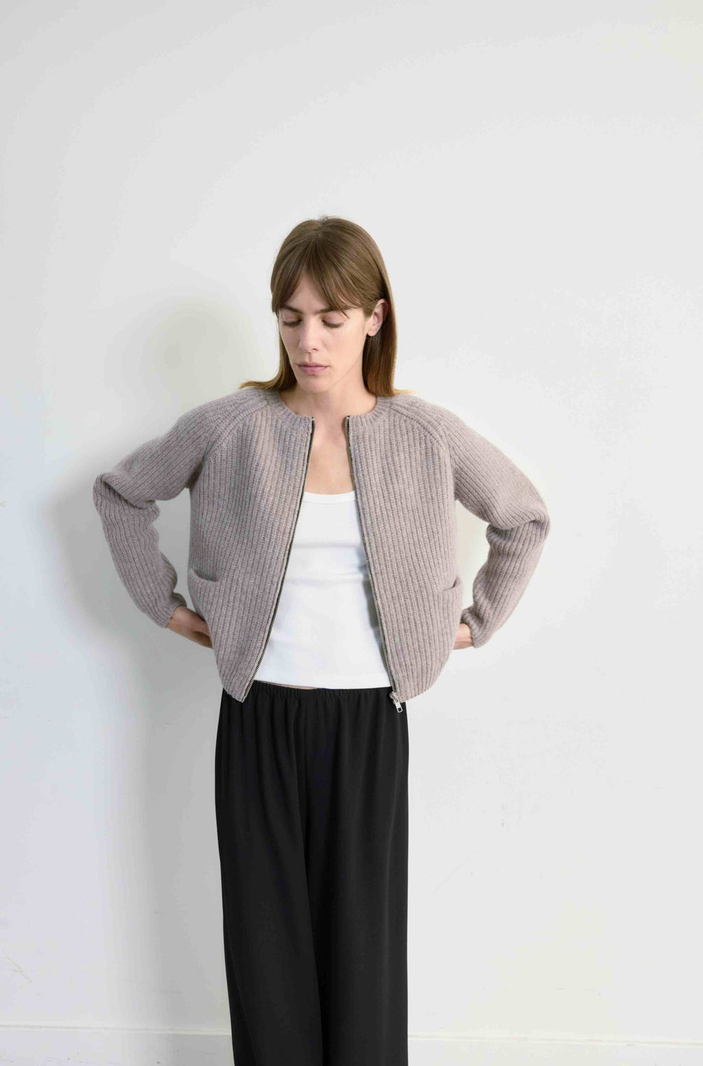 Woman wearing a light beige cardigan over a white top and black pants on a white background
