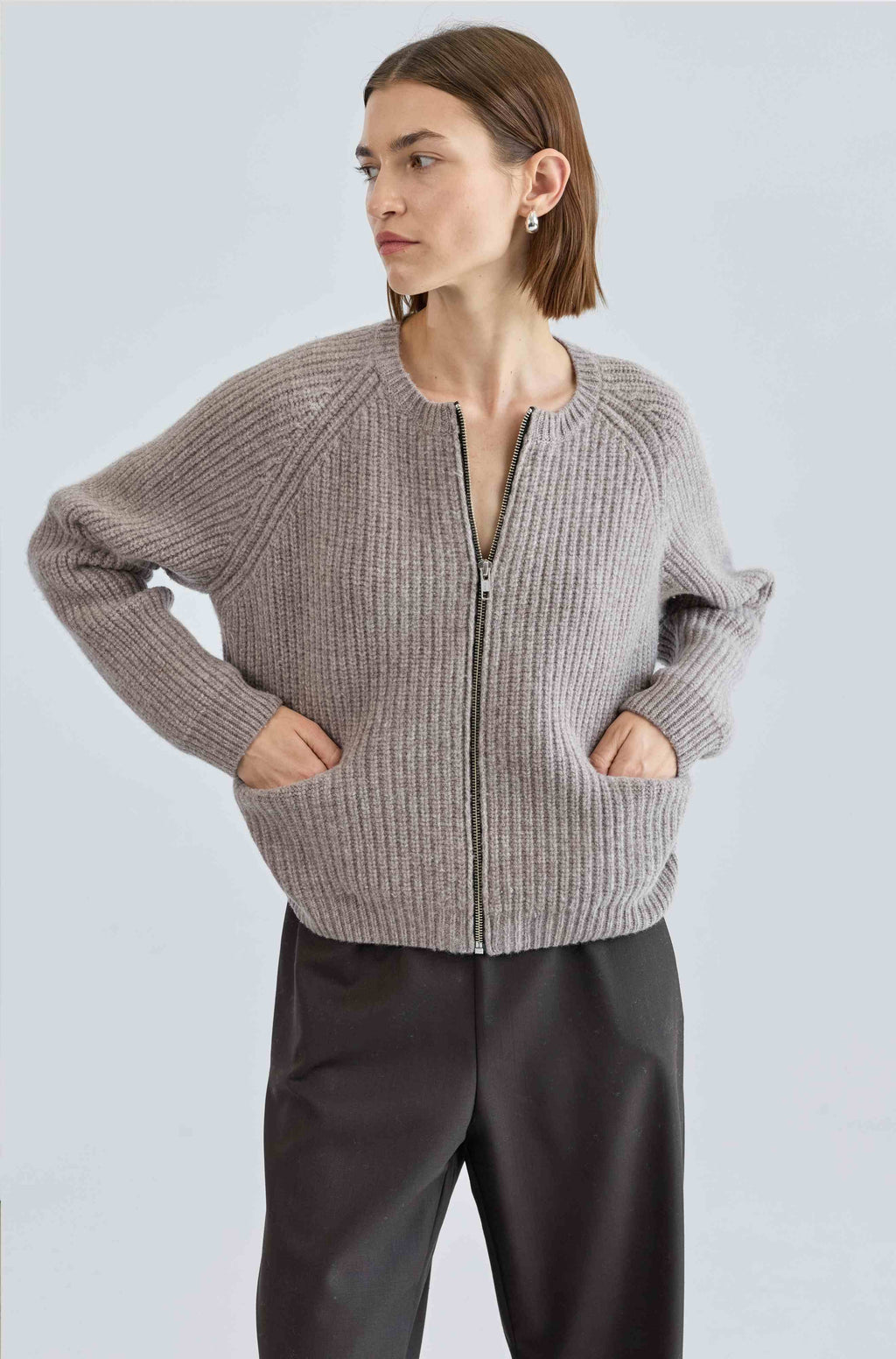 Woman wearing a light beige zip-up sweater against a light gray background