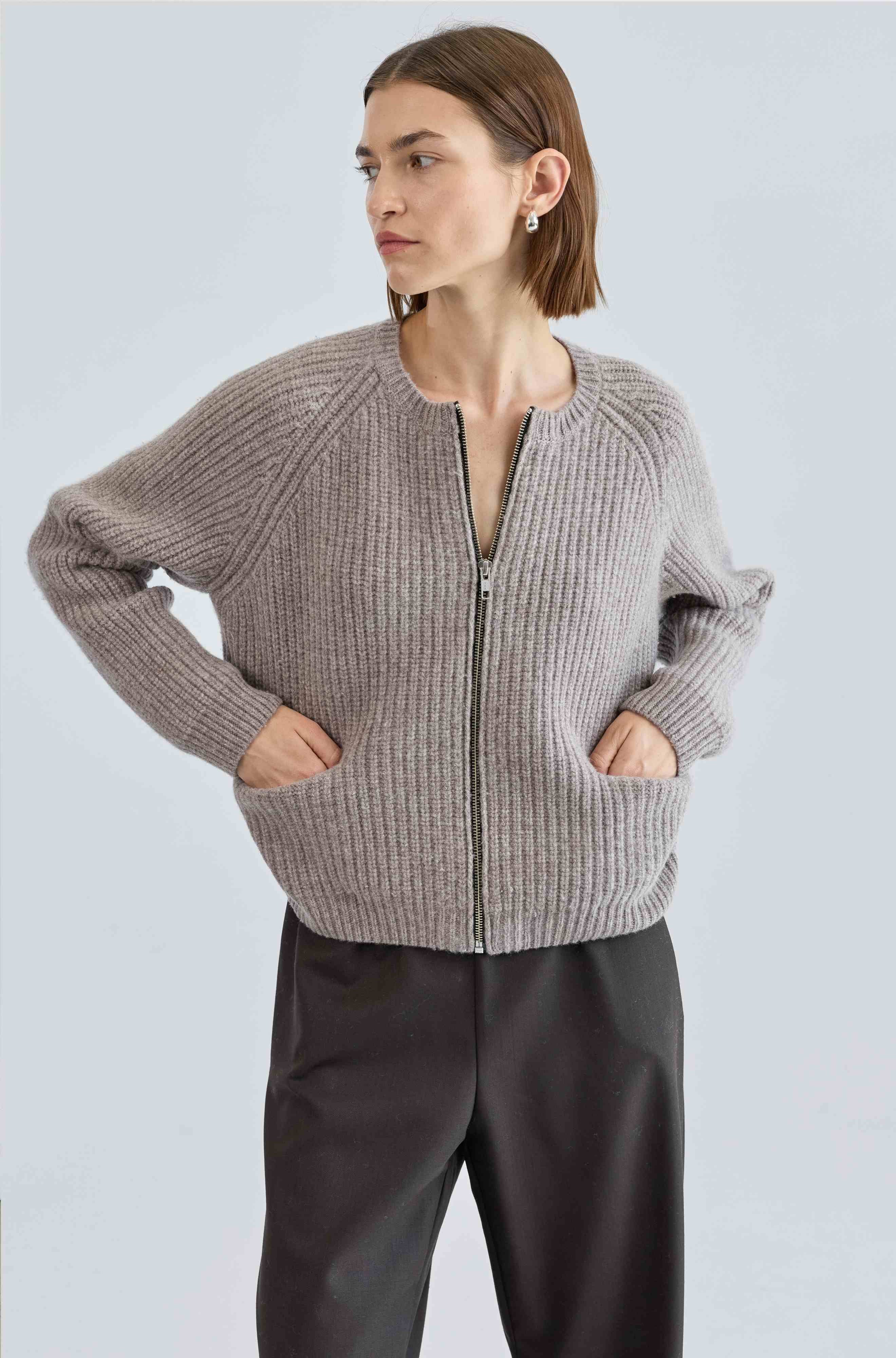 Woman wearing a light beige zip-up sweater against a light gray background