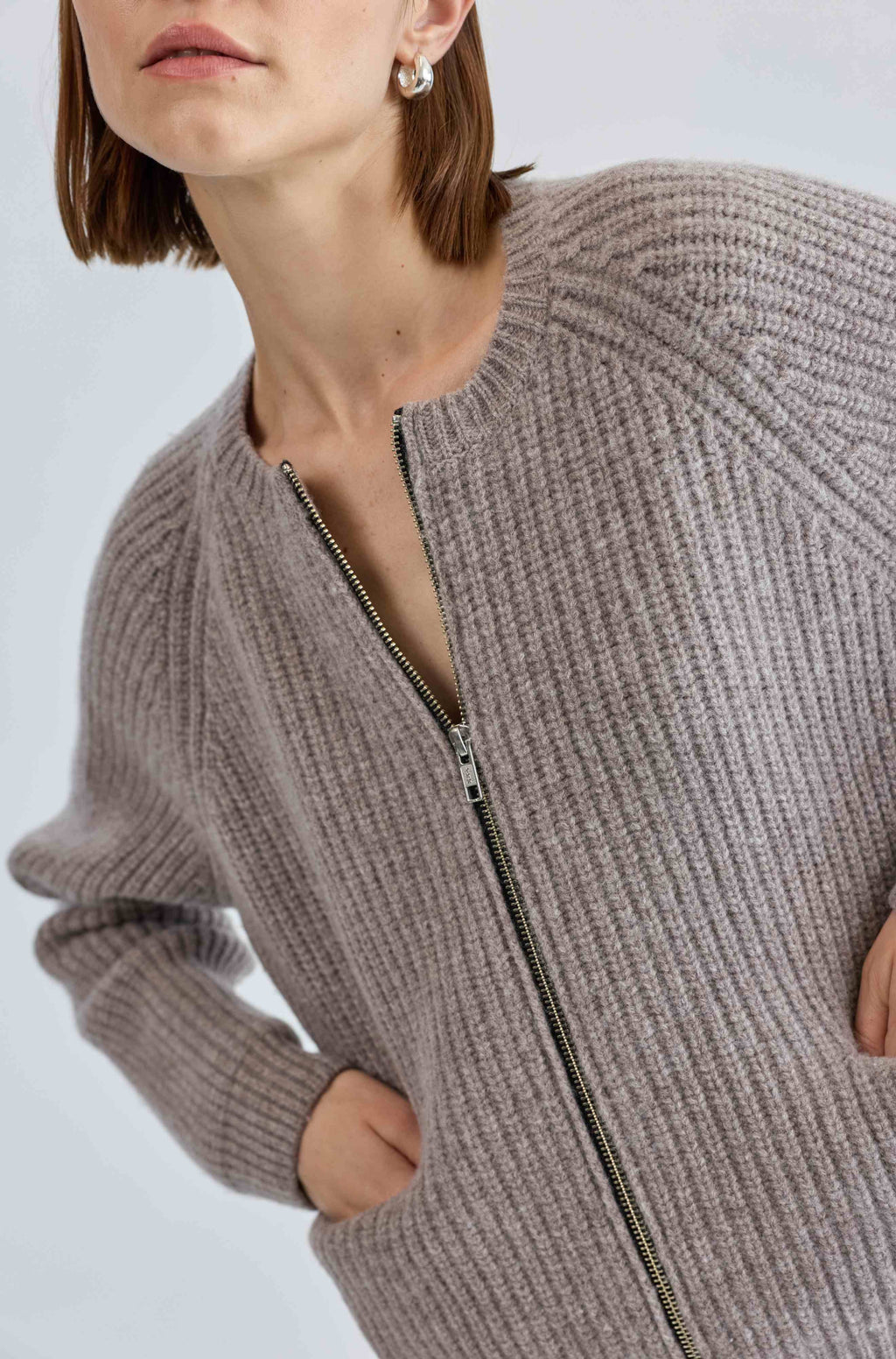 Close-up of a person wearing a ribbed knit cardigan with a zipper on a light gray background