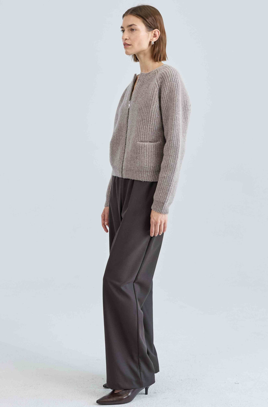 Woman wearing a ribbed zip-up cardigan and dark pants on a white background