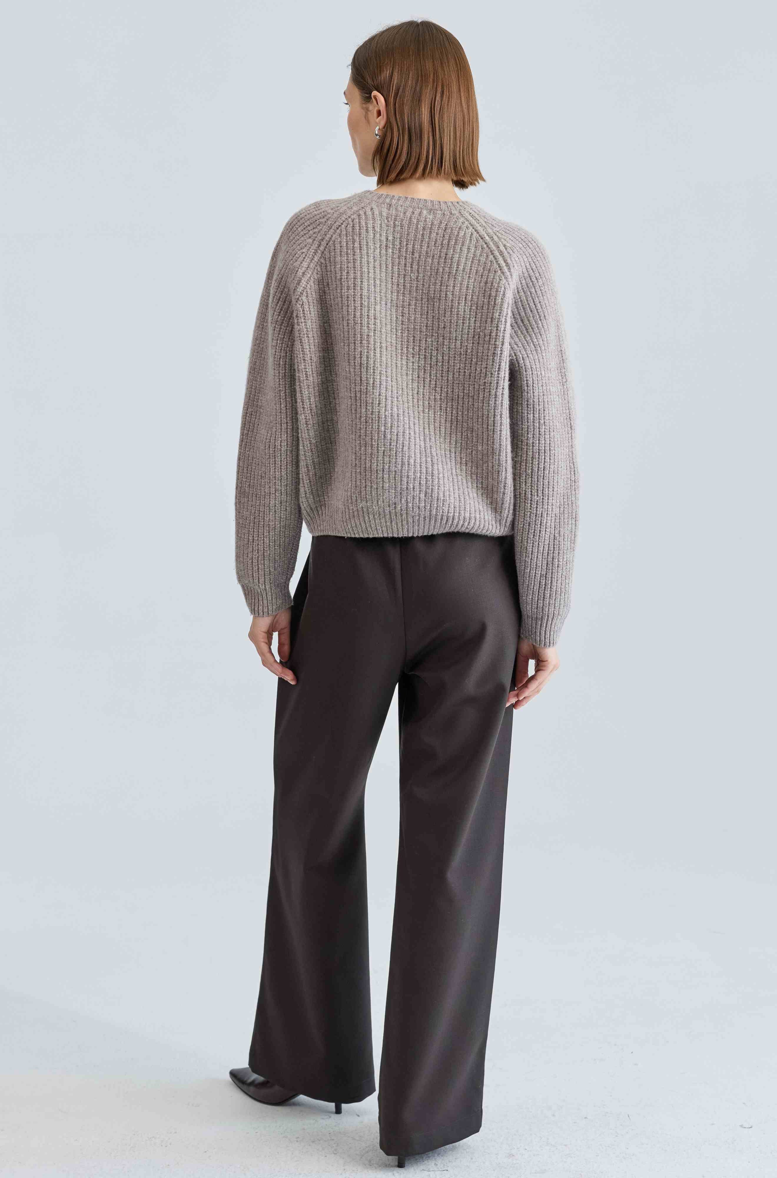 Person wearing a textured sweater and dark pants on a light gray background