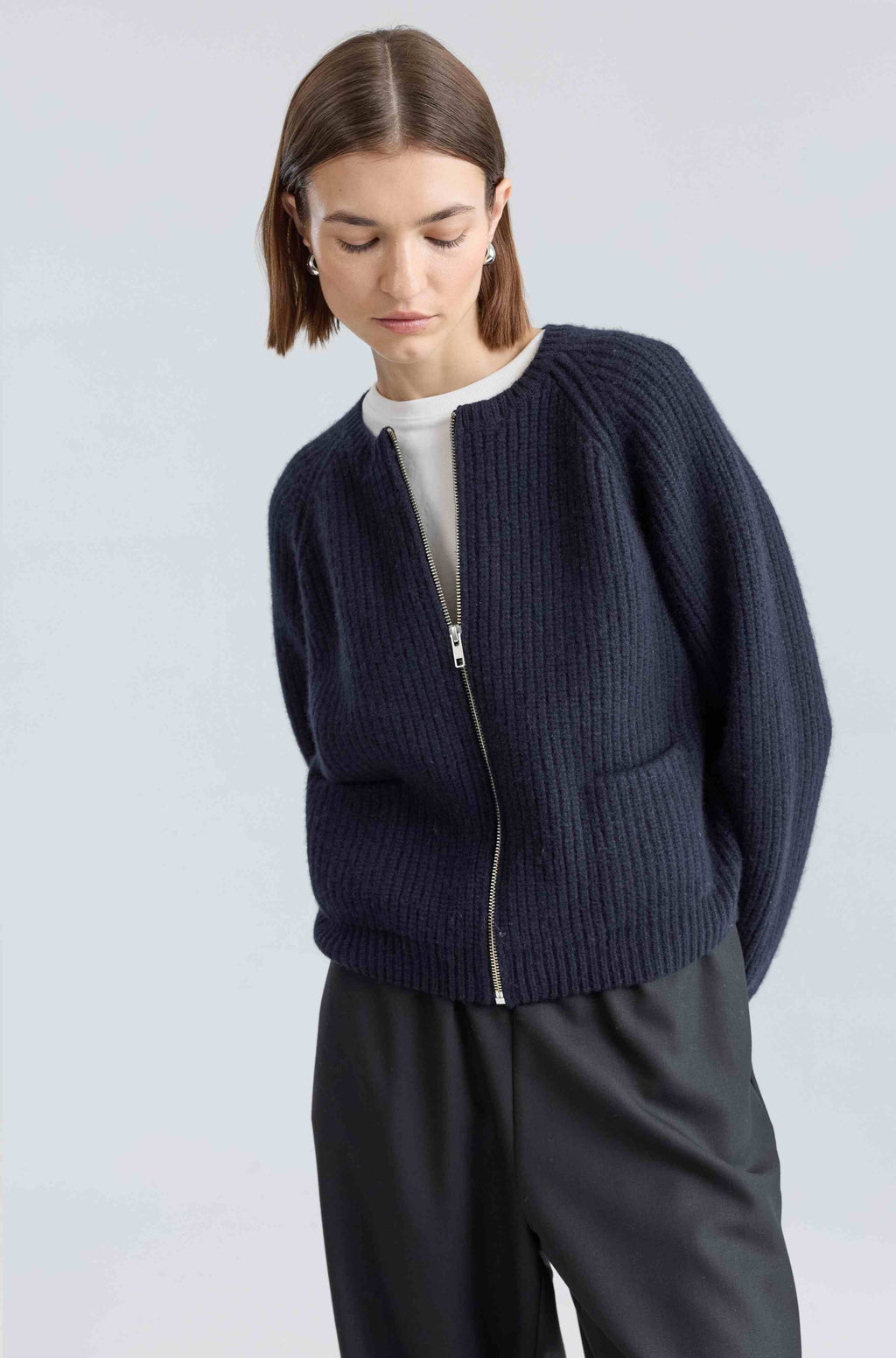 Woman wearing a navy blue zip-up sweater against a light gray background