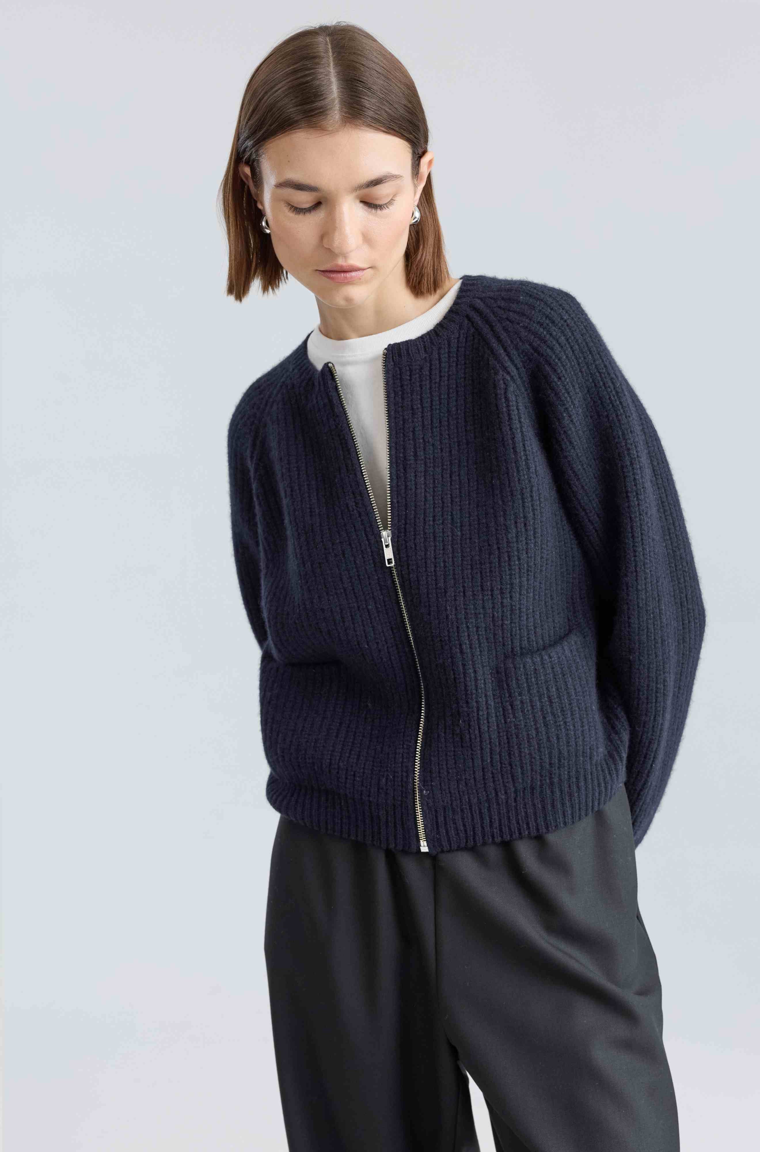 Woman wearing a navy blue zip-up sweater against a light gray background