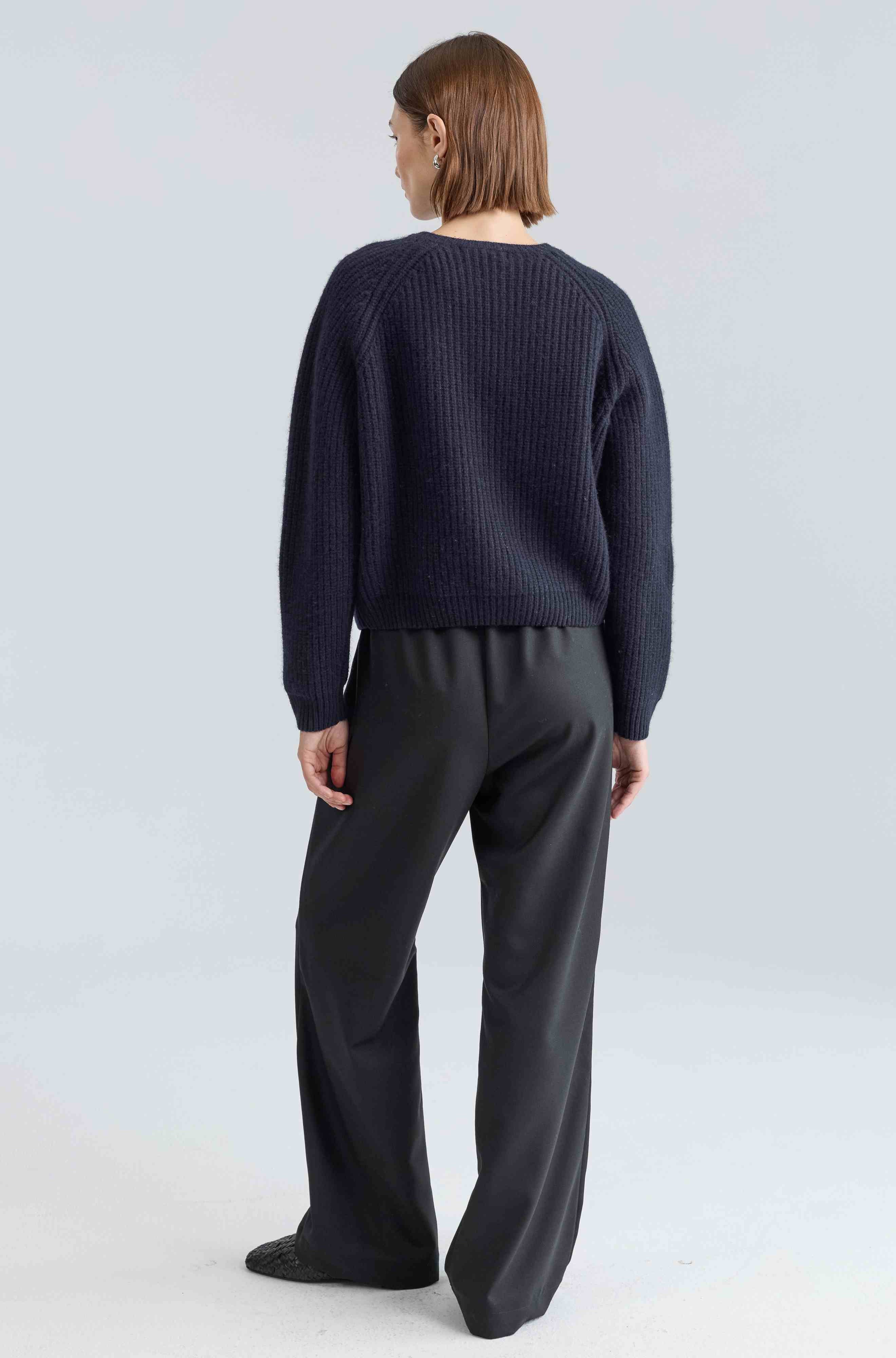 Person wearing a navy sweater and gray pants on a light gray background