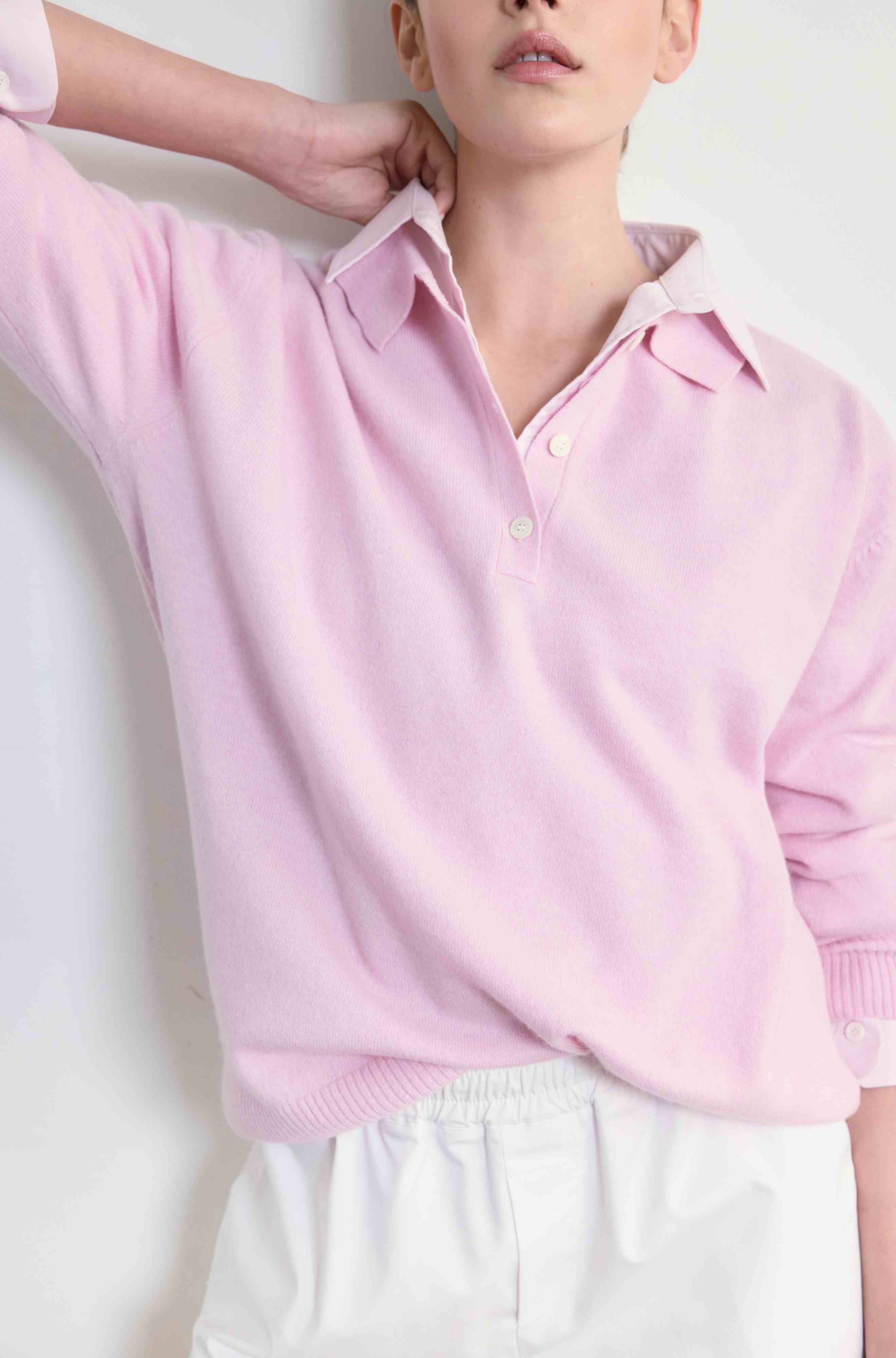 Person wearing a light pink collared shirt with a pink polo sweater on a white background