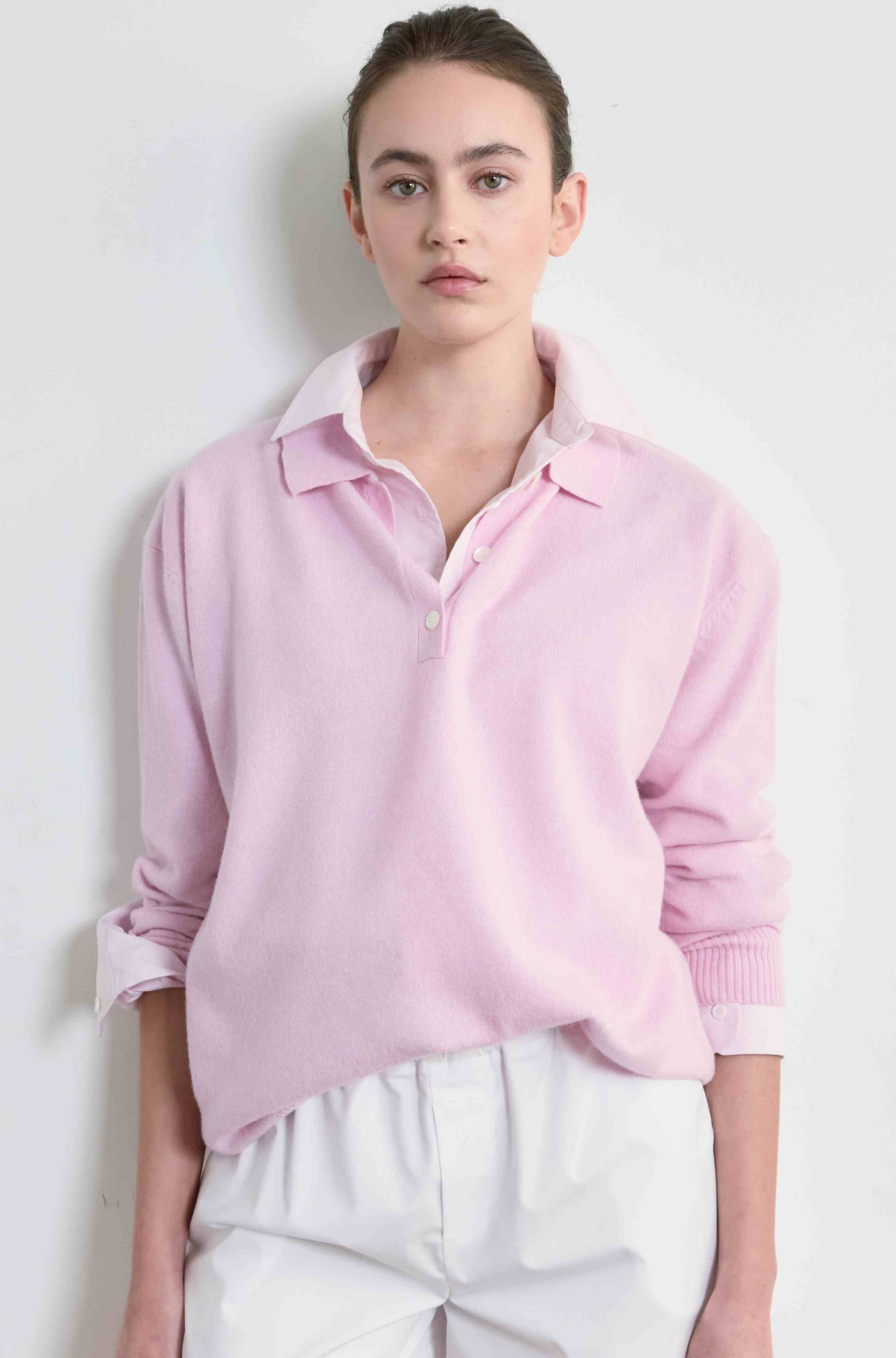 Person wearing a light pink sweater and white pants against a plain background