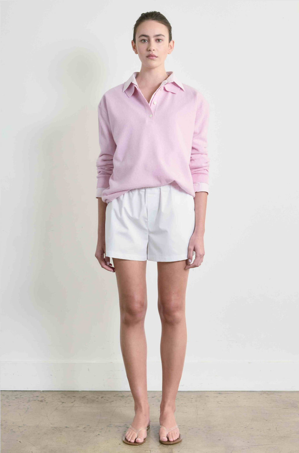 Person wearing a light pink sweater and white shorts against a plain background