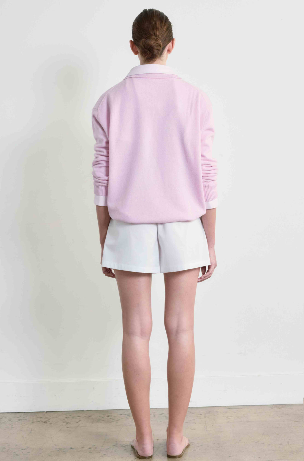Person wearing a light pink sweater and white shorts standing against a plain white background