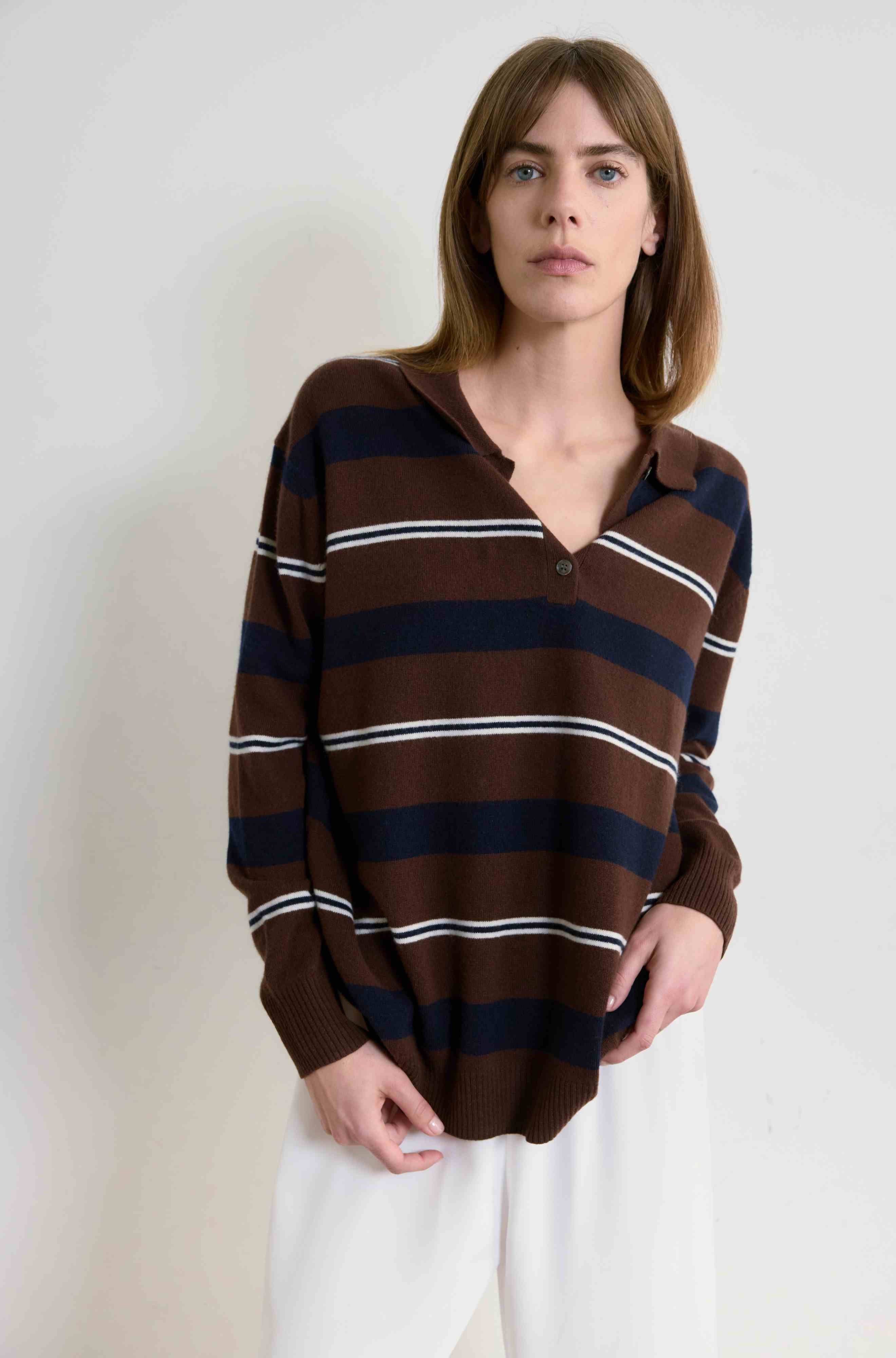 Woman wearing a brown, navy, and white striped sweater against a plain background
