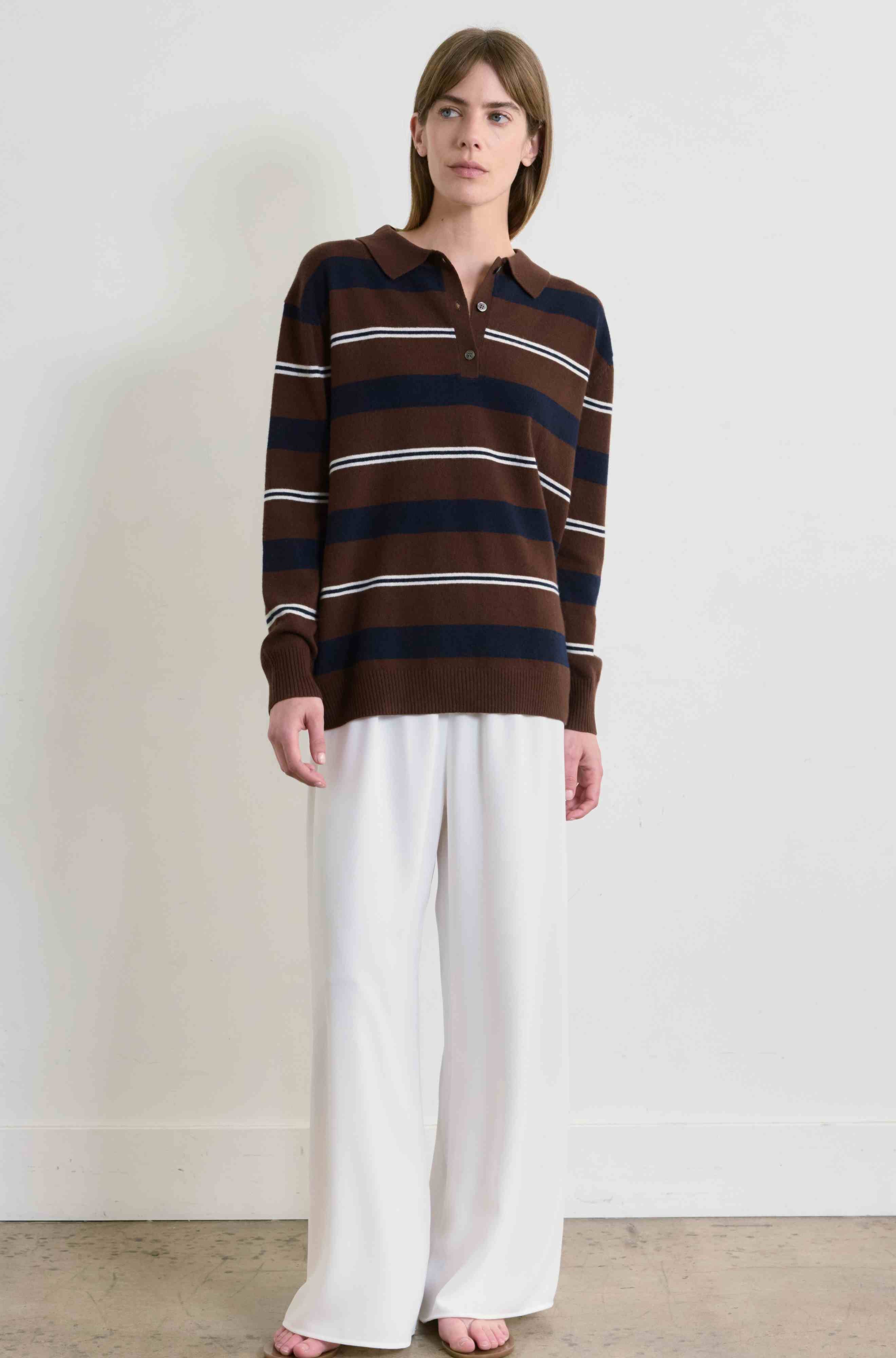 Person wearing a brown and navy striped shirt with white pants on a plain background