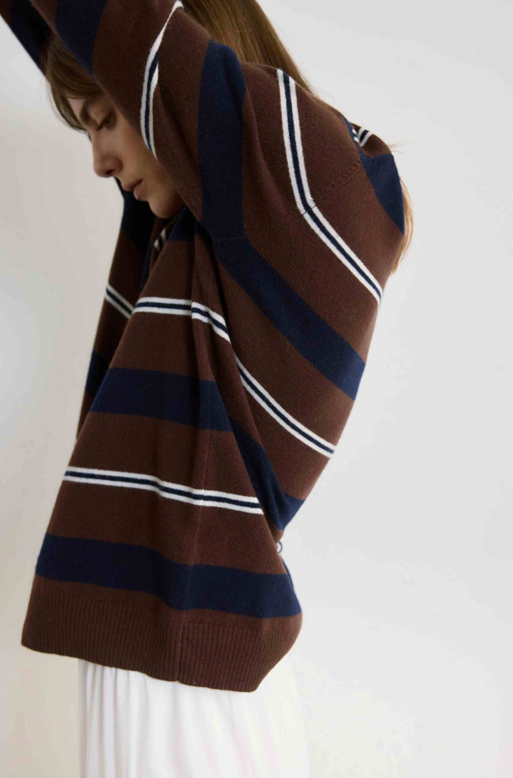 Person wearing a brown, navy, and white striped sweater with a hood on a plain background